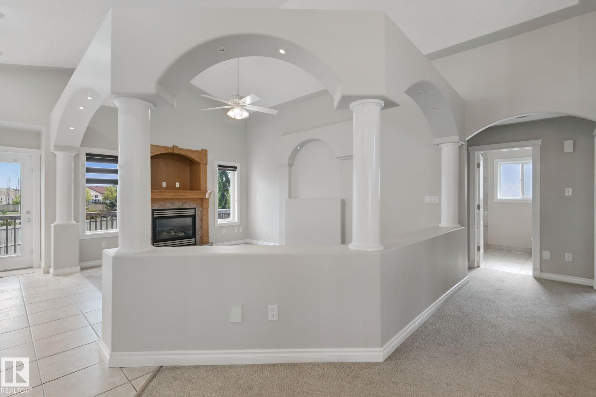 Integrated fireplace with wood surround, arched architectural details, recessed lighting, ceiling fan, and tiled flooring - 16807 78 Street Nw, Edmonton, AB