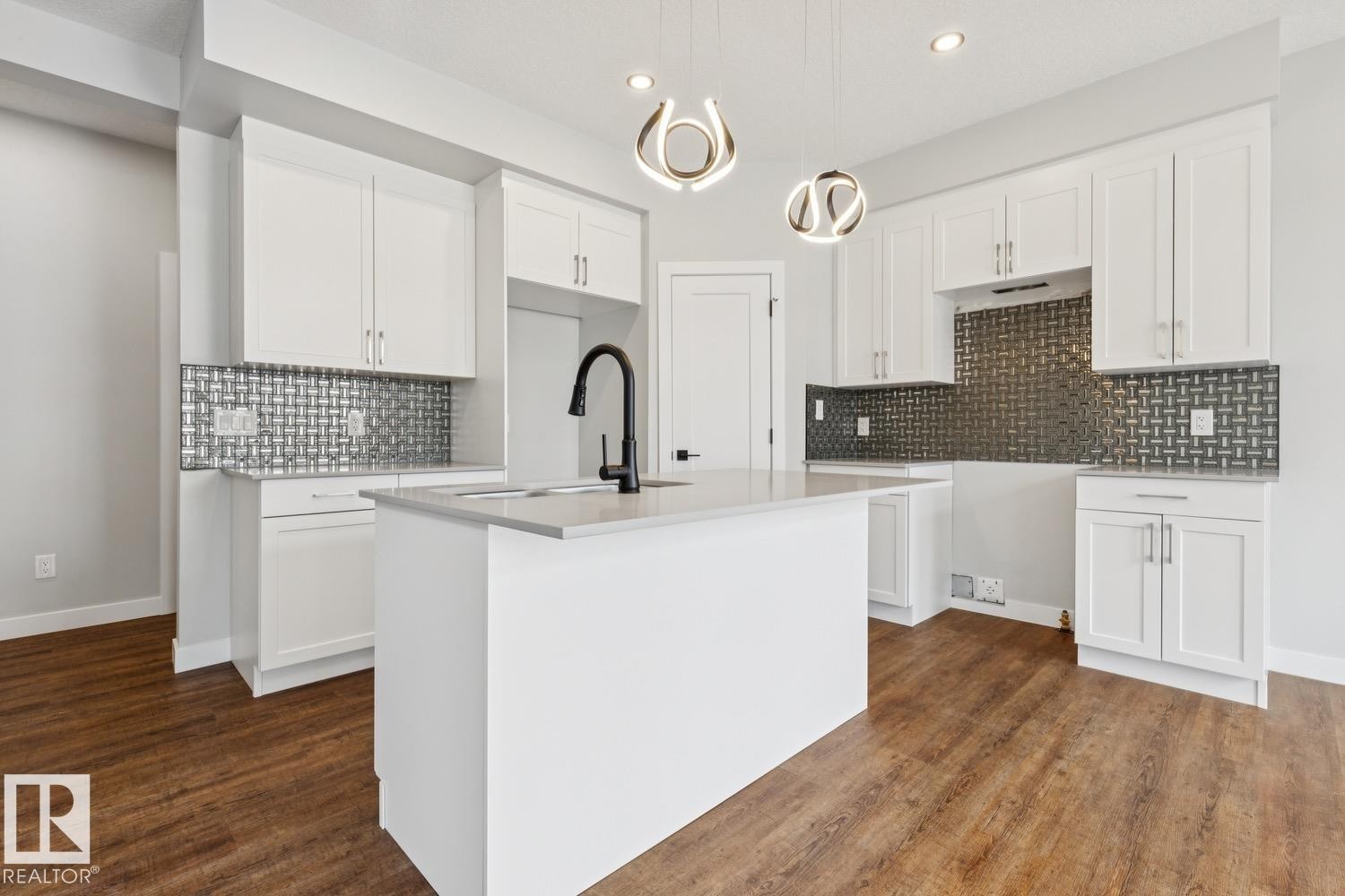 White cabinetry, a center island with sink, dark wood-finish flooring, mosaic tile backsplash, and contemporary pendant lighting - 72 Maple Crescent, Gibbons, AB