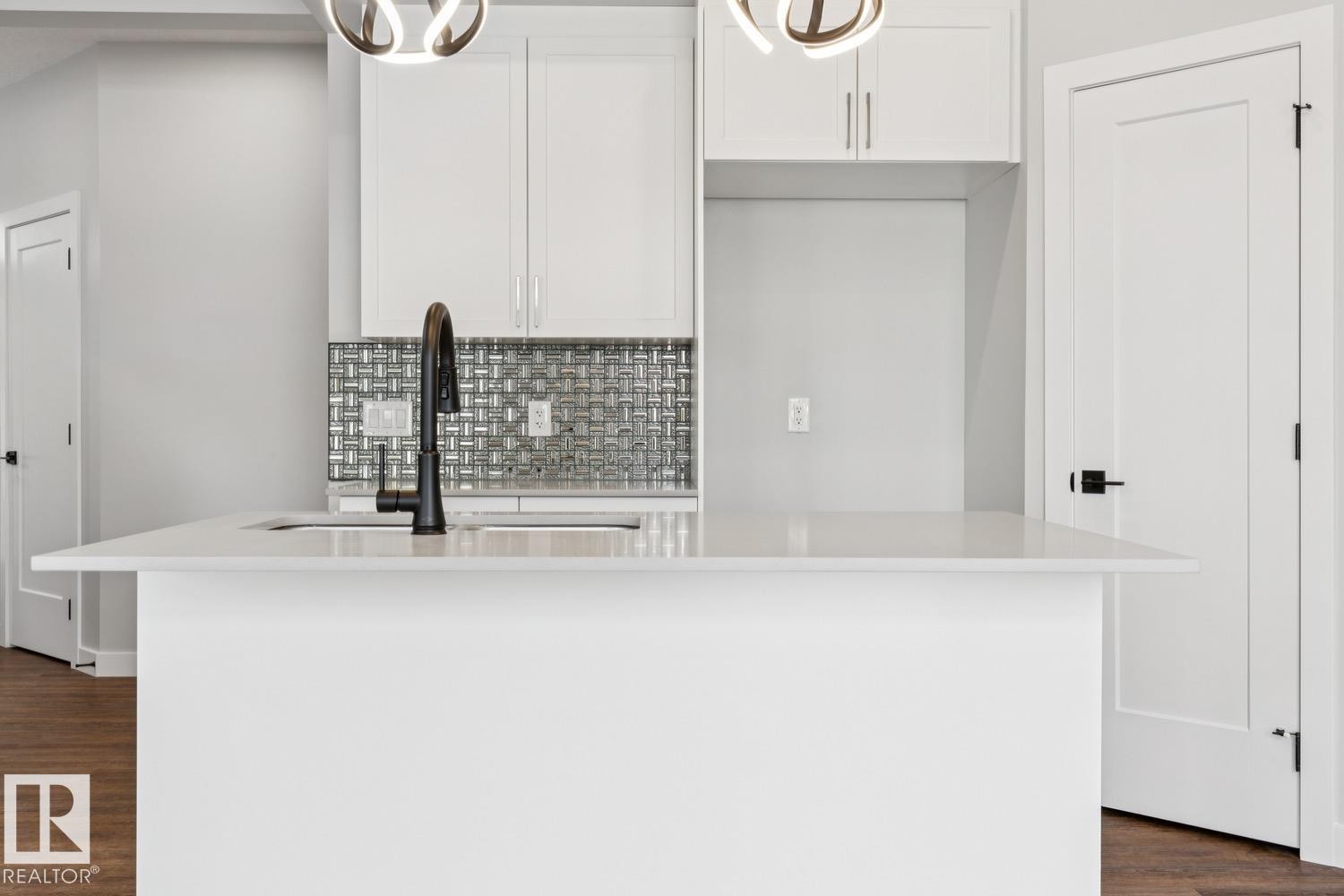 Kitchen island featuring a single-basin sink with a matte black faucet, white cabinetry, and a textured tile backsplash - 72 Maple Crescent, Gibbons, AB
