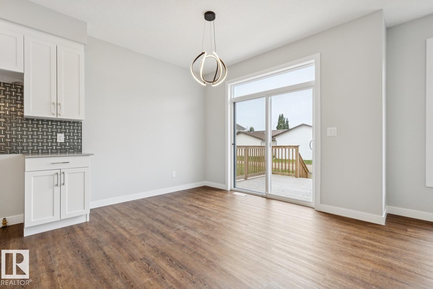 White cabinetry with a light stone-finish countertop, dark mosaic tile backsplash, wood-finish flooring, and a contemporary ceiling light fixture - 72 Maple Crescent, Gibbons, AB