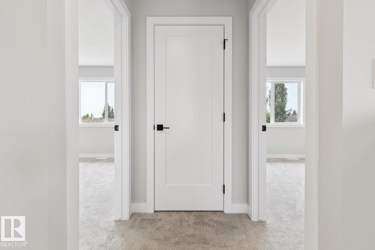 Hallway featuring light gray carpeting, white flat-panel doors with matte black hardware, and bright interior spaces with windows - 72 Maple Crescent, Gibbons, AB