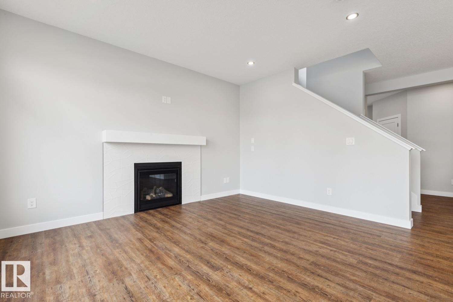 Living space featuring a built-in fireplace with a white mantel, wood-finish flooring, and recessed lighting - 72 Maple Crescent, Gibbons, AB
