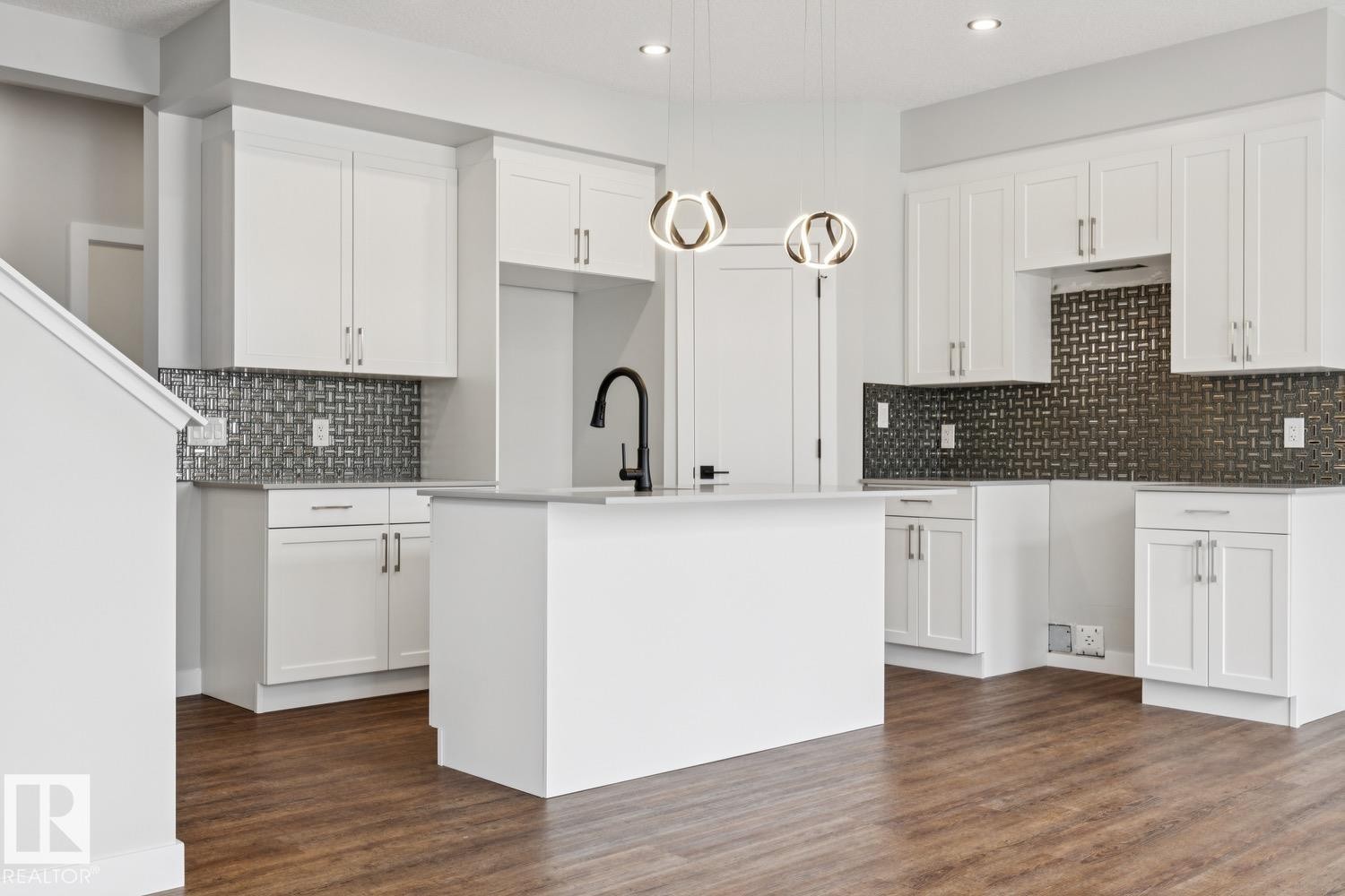 Kitchen featuring white shaker cabinetry, an expansive center island, dark patterned tile backsplash, wood-finish flooring, and contemporary pendant lighting - 72 Maple Crescent, Gibbons, AB