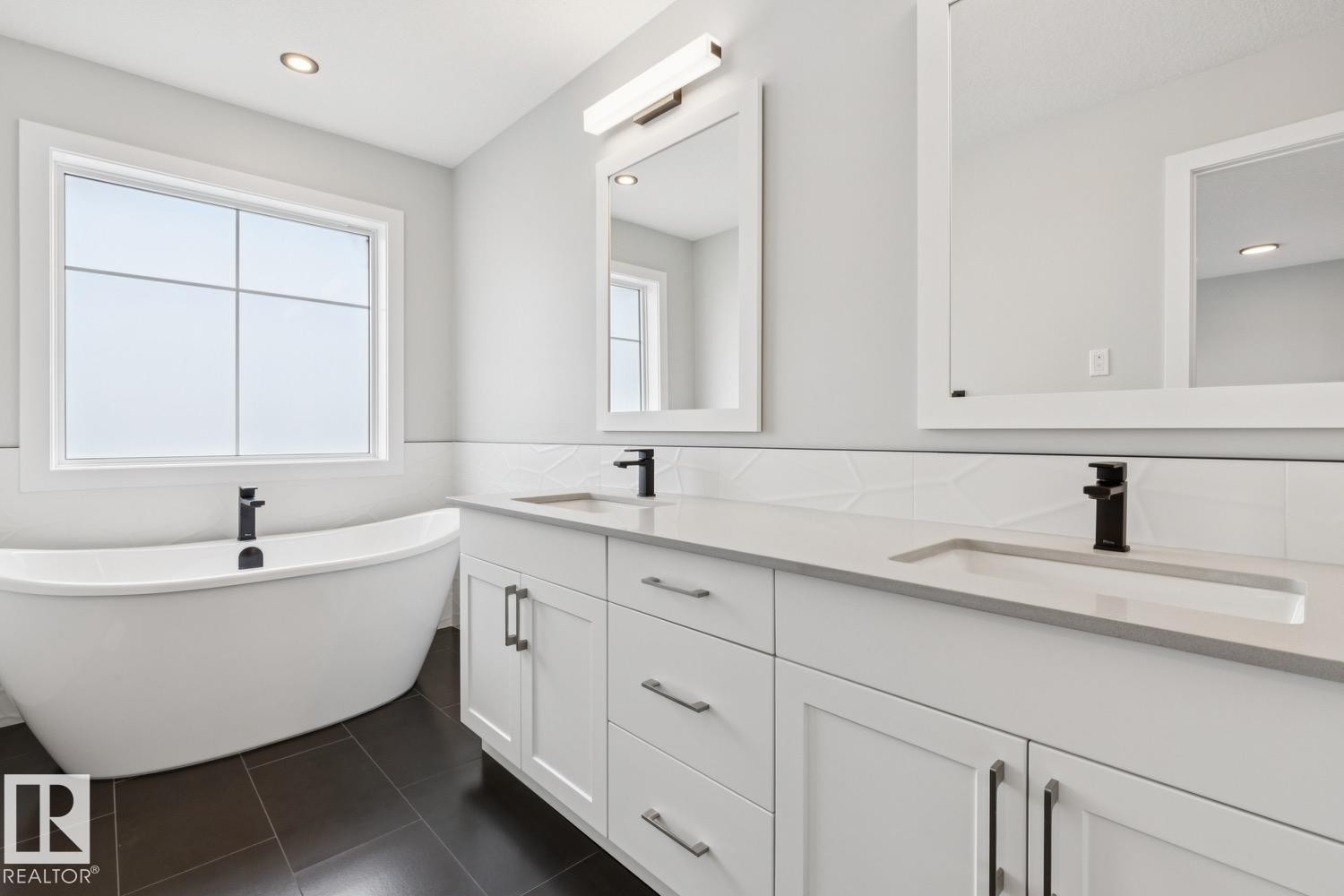 Freestanding soaking tub, dual vanity with undermount sinks, quartz countertops, black plumbing fixtures, and dark tile flooring - 72 Maple Crescent, Gibbons, AB