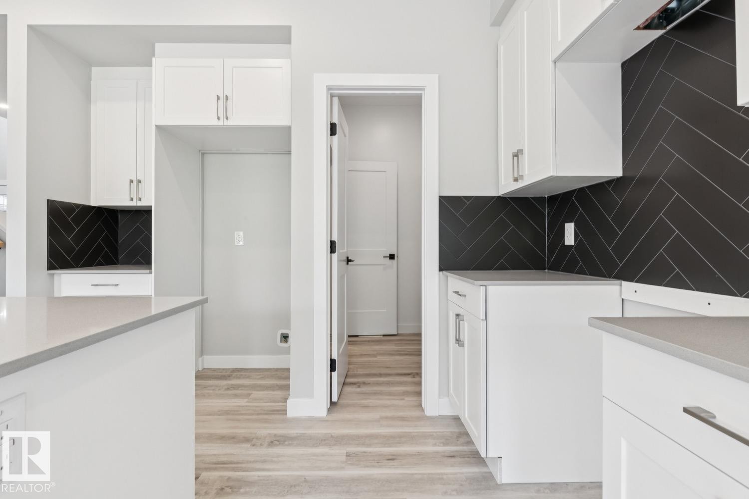 White shaker-style cabinetry with chrome hardware, light-toned countertops, dark herringbone tile backsplash, and wood-finish flooring - 36 Maple Crescent, Gibbons, AB