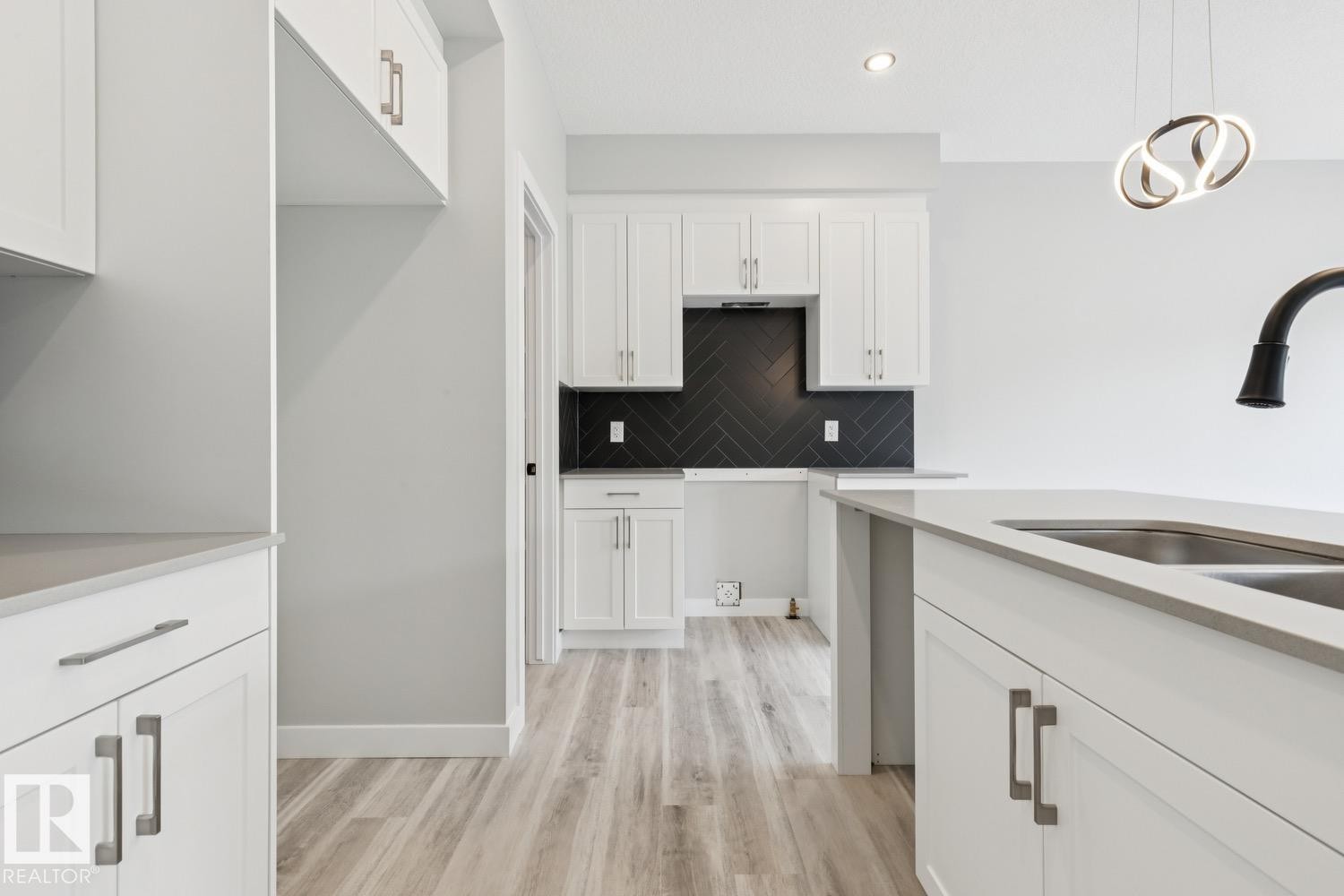 Contemporary kitchen featuring white cabinetry, wood-finish flooring, a herringbone tile backsplash, a kitchen island with an undermount sink, and recessed lighting - 36 Maple Crescent, Gibbons, AB