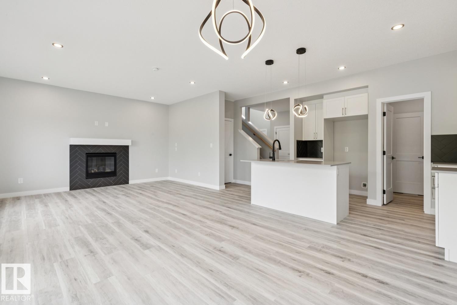 Open-concept living space featuring light wood-finish flooring throughout, a modern linear ceiling fixture, and abundant recessed lighting - 36 Maple Crescent, Gibbons, AB