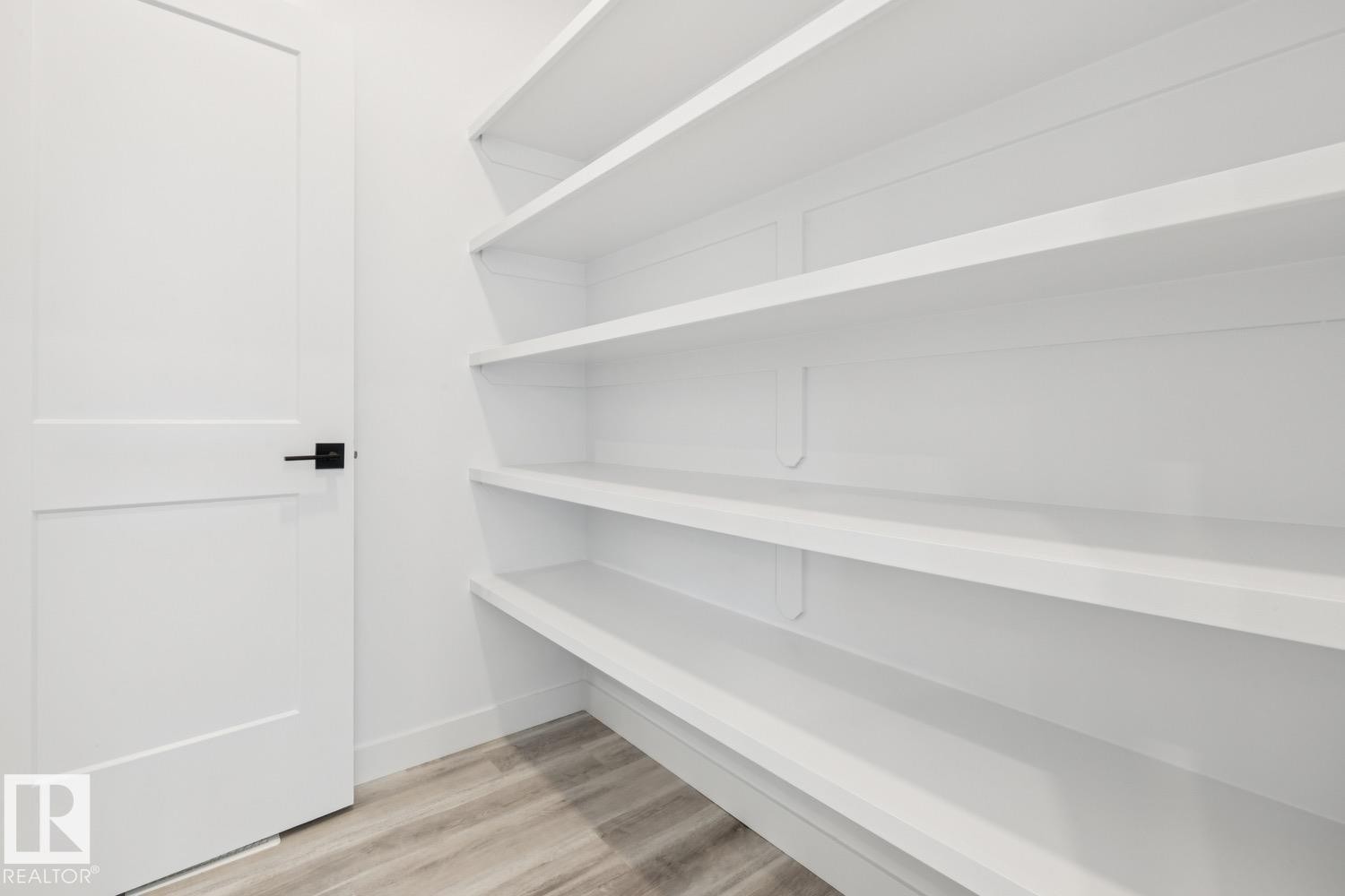 Built-in shelving with white finishes, a panel door with matte black hardware, and wood-finish flooring - 36 Maple Crescent, Gibbons, AB