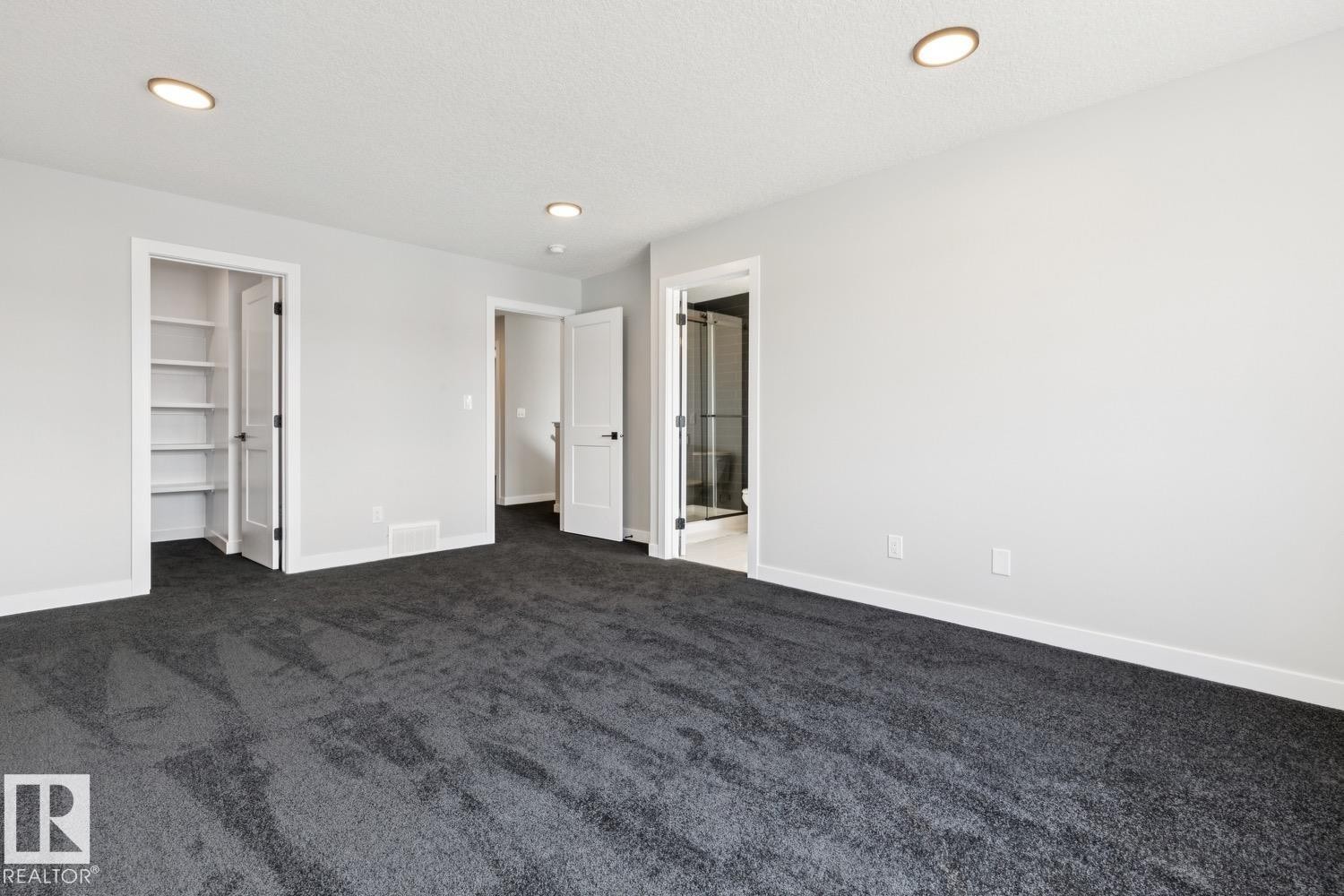 Spacious room with dark gray carpeting, recessed ceiling lighting, and multiple white panel doors - 36 Maple Crescent, Gibbons, AB