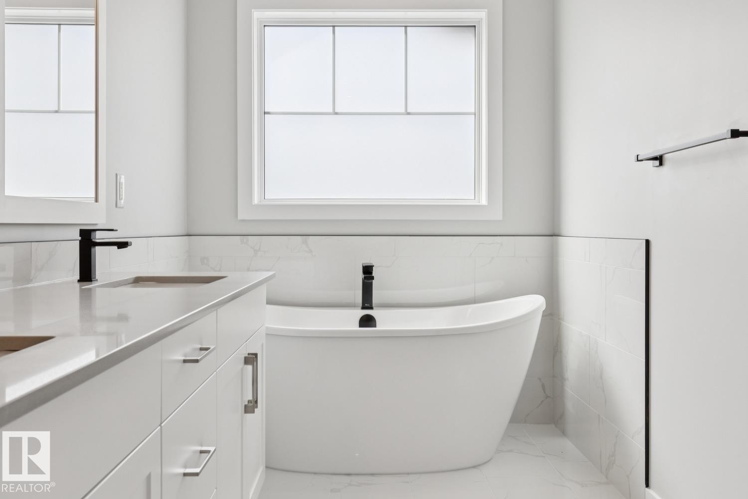 Freestanding soaking tub, dual vanity with undermount sinks, quartz countertop, matte black fixtures, and white tiled walls - 36 Maple Crescent, Gibbons, AB