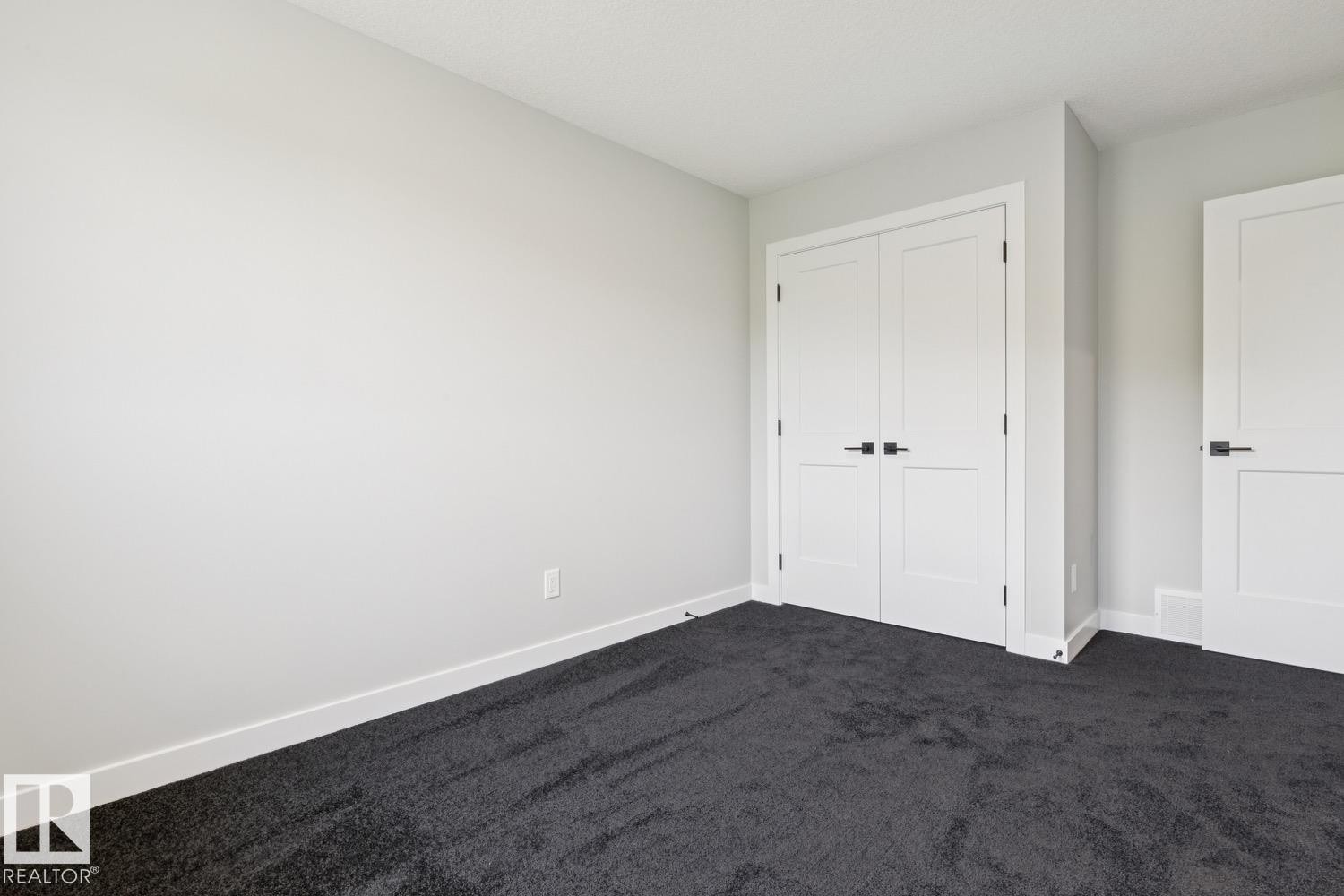 Neutral wall paint, dark carpet, white trim, and white doors with matte black hardware - 36 Maple Crescent, Gibbons, AB