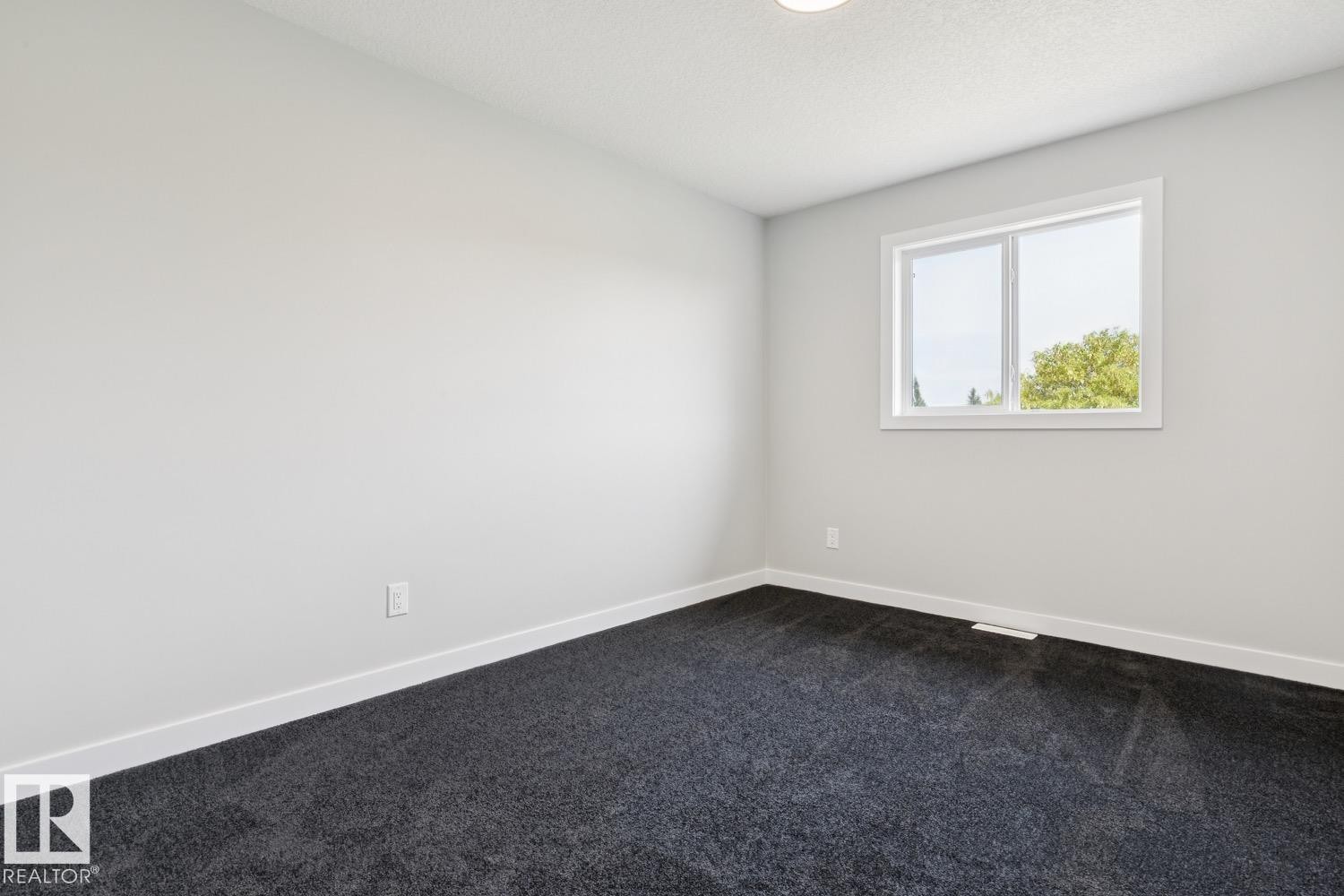 Clean-lined room featuring light gray walls, dark gray carpeting, and a white-framed window - 36 Maple Crescent, Gibbons, AB