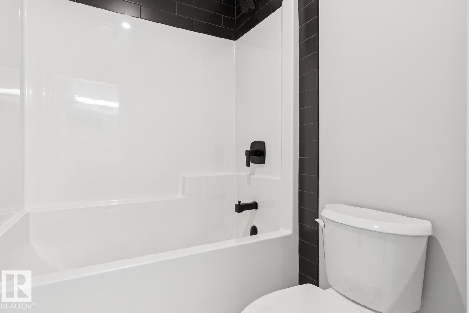White bathtub with matte black fixtures and a tiled surround - 36 Maple Crescent, Gibbons, AB