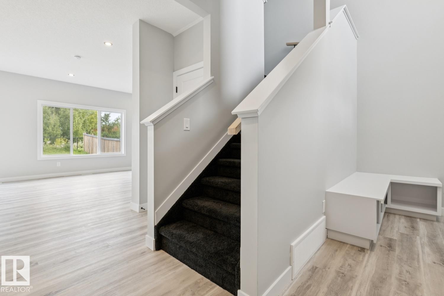 Staircase with dark carpeted treads, wood-finish flooring, recessed lighting, and a built-in storage bench - 36 Maple Crescent, Gibbons, AB