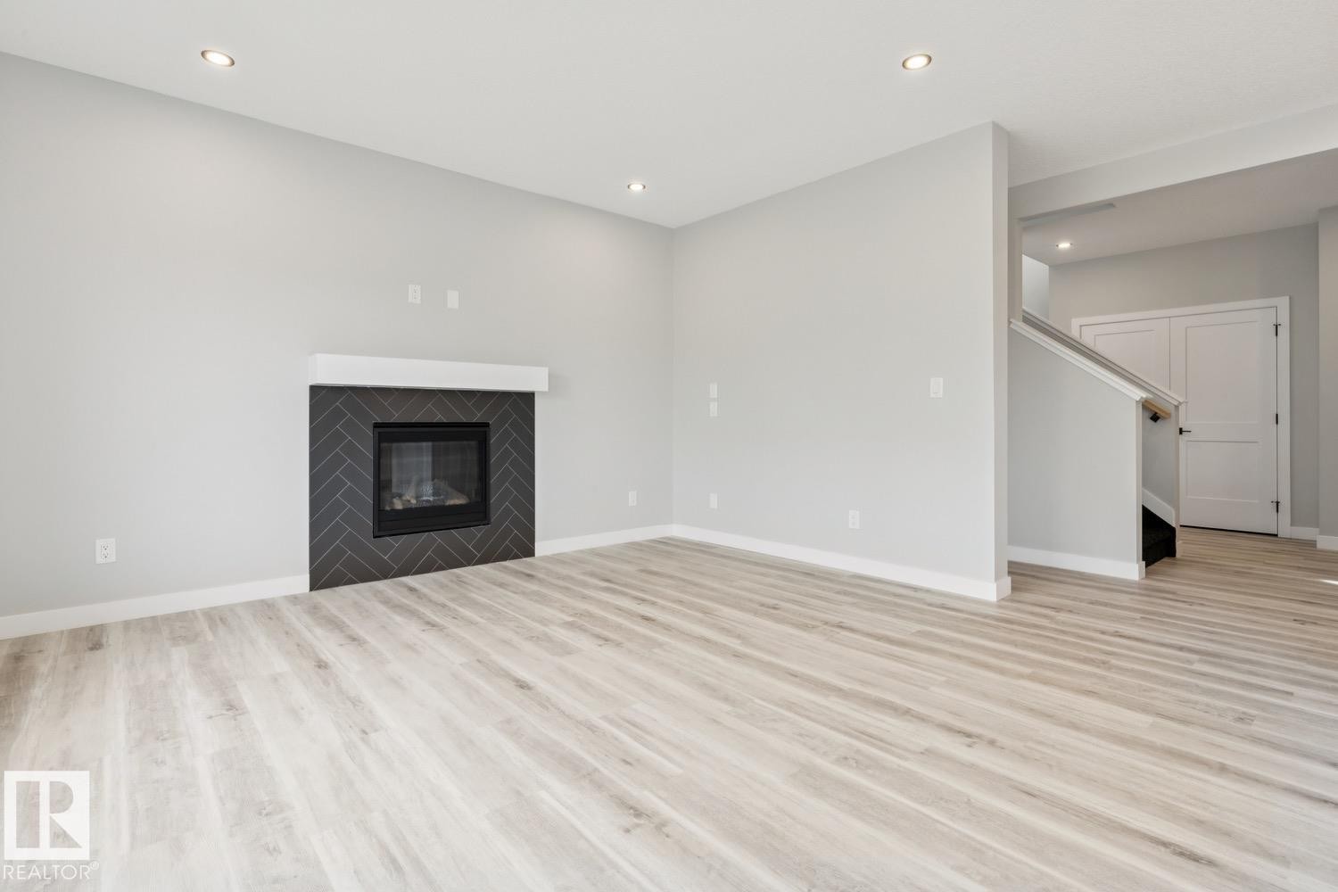 Wood-finish flooring throughout, modern fireplace with a herringbone tile surround, white mantel, recessed lighting, and a staircase with a wooden handrail - 36 Maple Crescent, Gibbons, AB