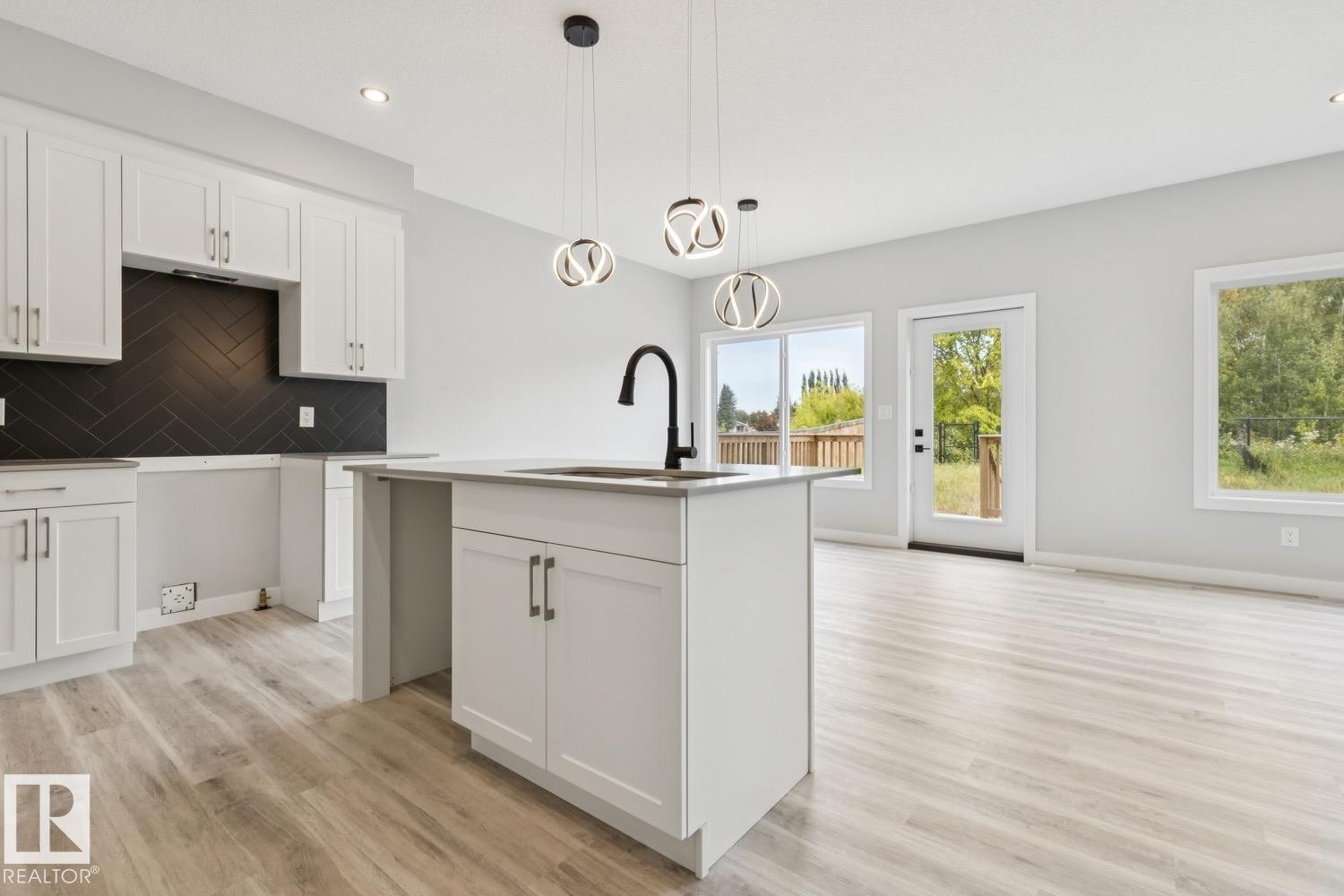 Kitchen island with an undermount sink and matte black faucet, surrounded by white cabinetry and a dark herringbone tile backsplash - 36 Maple Crescent, Gibbons, AB