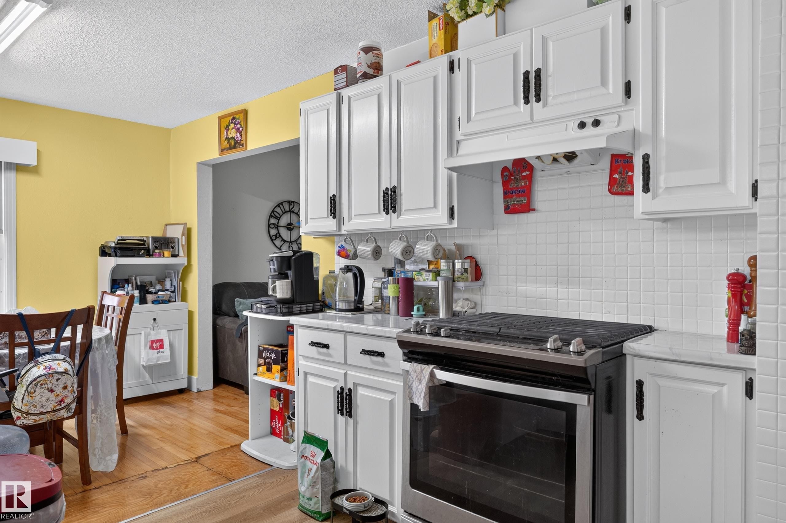 White cabinetry with black hardware, white tile backsplash, light-colored countertops, stainless steel range, and wood-finish flooring - 12309 80 Street Nw, Edmonton, AB