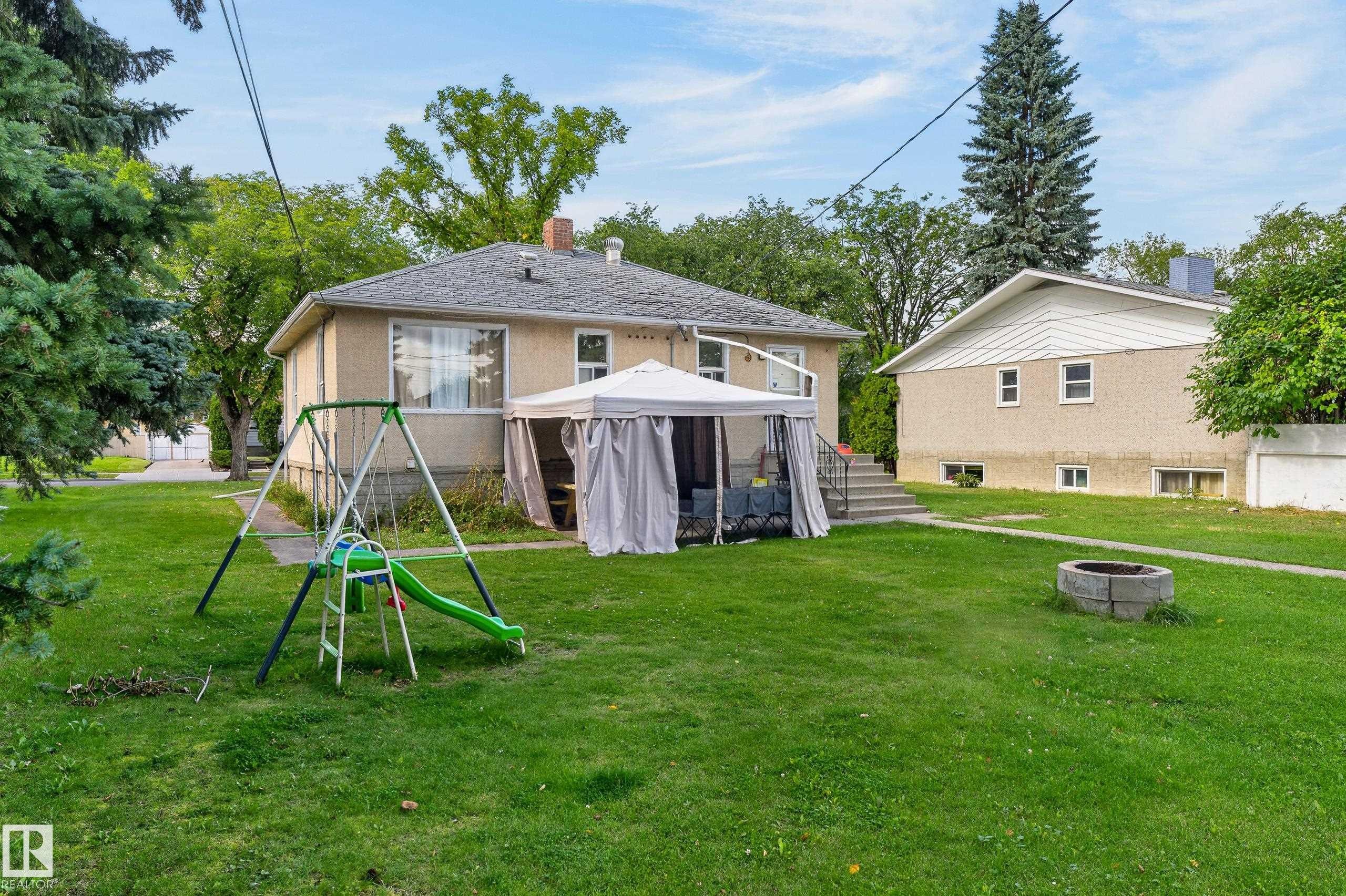 Expansive green lawn with mature trees, a stone fire pit, and concrete steps to the rear entry - 12345 79 Street Nw, Edmonton, AB