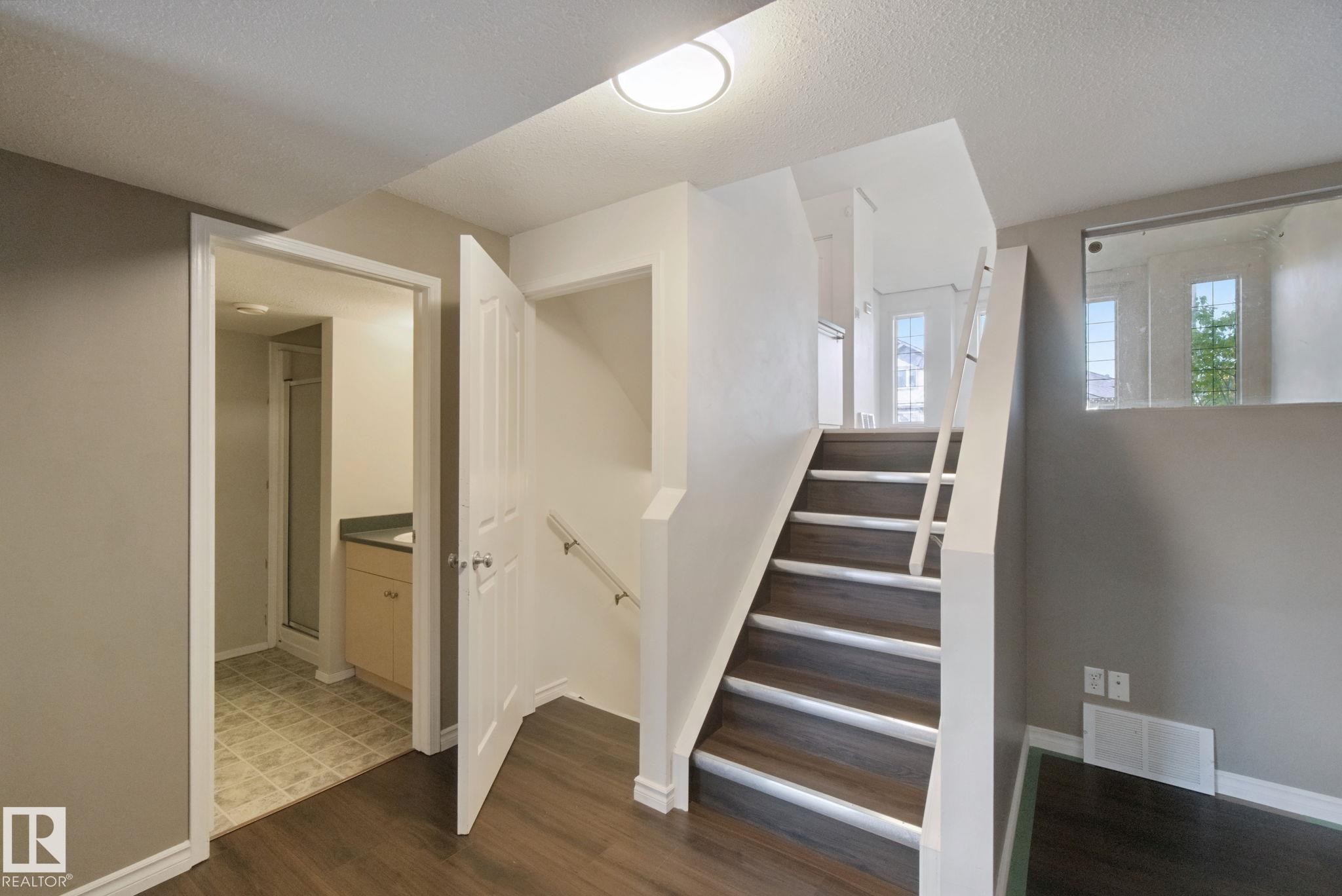 Wood-finish flooring, staircase with white risers, glass panel railing, and built-in vanity with countertop - 2117 36 Avenue Nw, Edmonton, AB