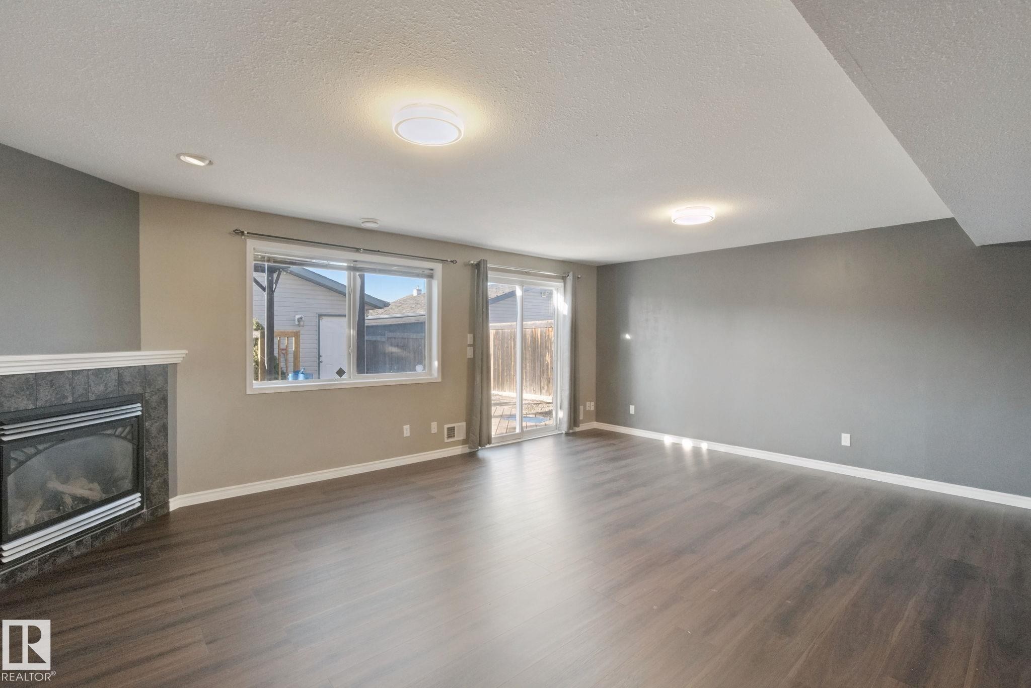 Living area featuring wood-finish flooring, a fireplace with a tiled surround and mantel, and a sliding glass door - 2117 36 Avenue Nw, Edmonton, AB