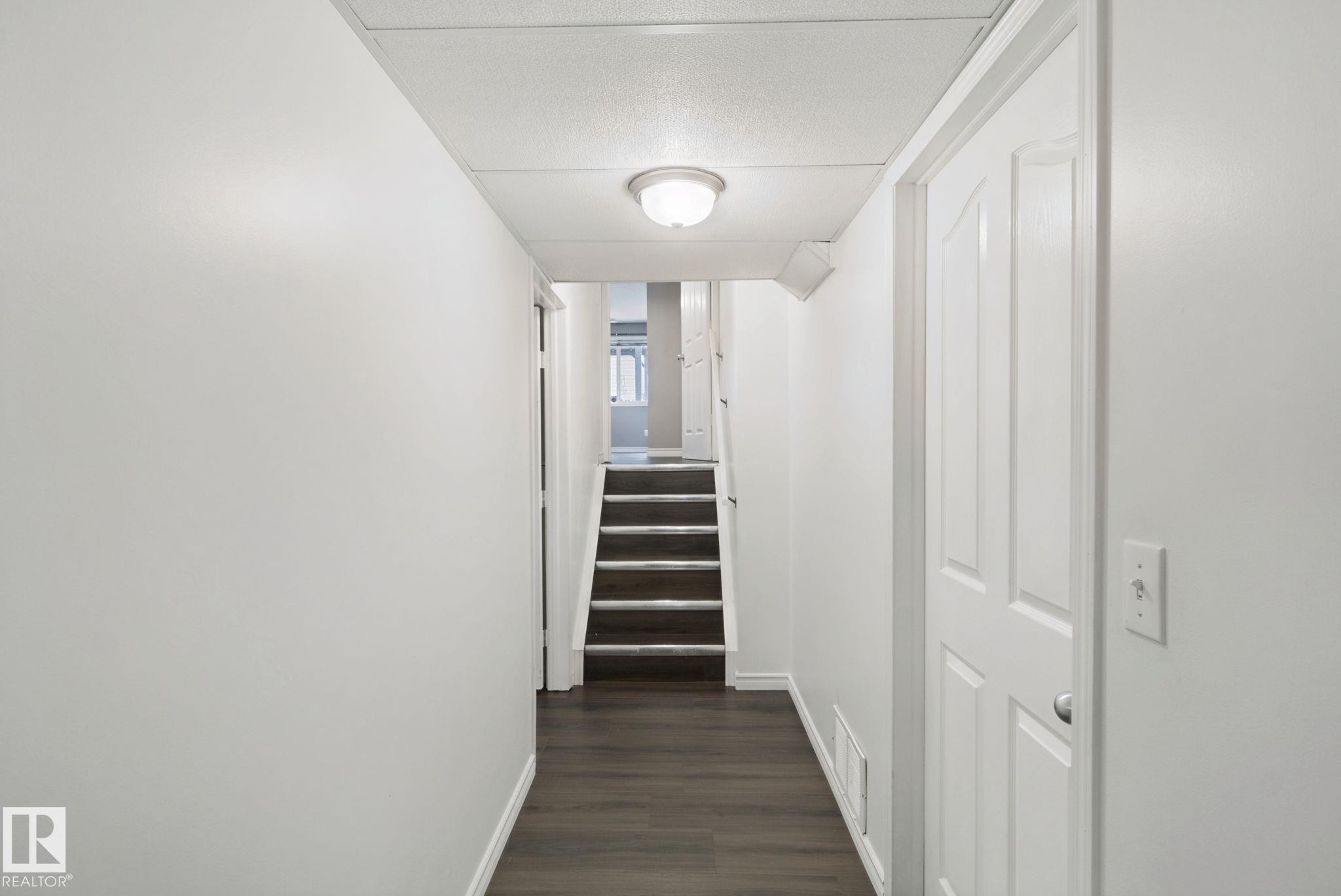 Hallway featuring dark wood-finish flooring, light-toned walls, a flush-mount ceiling light, and a paneled interior door - 2117 36 Avenue Nw, Edmonton, AB