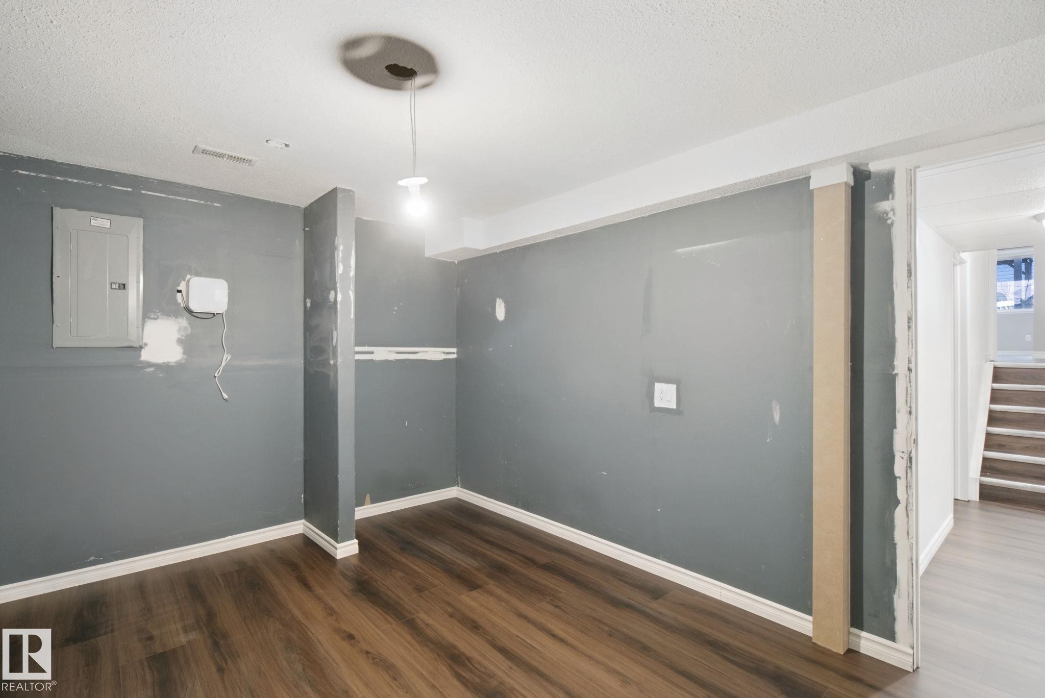 Wood-finish flooring with white trim, electrical panel, and exposed ceiling light fixture - 2117 36 Avenue Nw, Edmonton, AB