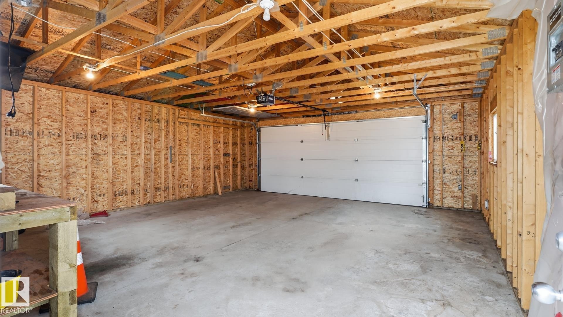 Spacious garage with exposed wood beam ceiling, concrete flooring, automatic garage door opener, and overhead lighting - 2117 36 Avenue Nw, Edmonton, AB