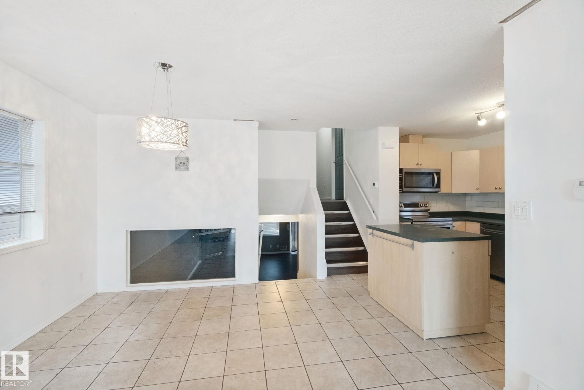 Open-concept living area with tile flooring, a built-in fireplace, and a kitchen featuring a peninsula island, light wood-finish cabinetry, and stainless steel appliances - 2117 36 Avenue Nw, Edmonton, AB