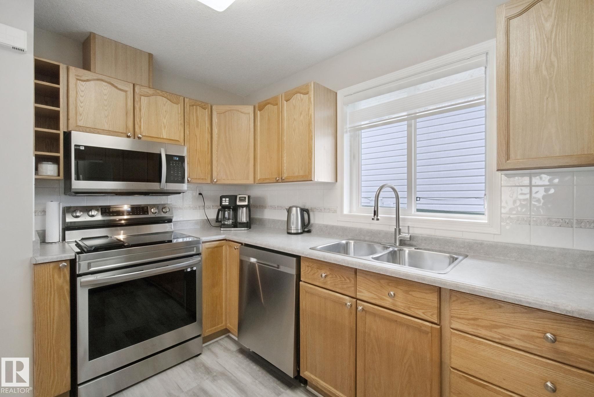 Kitchen featuring stainless steel appliances, wood-finish cabinetry, a double basin sink, light-toned countertops, and tile backsplash - 13912 156 Avenue Nw, Edmonton, AB
