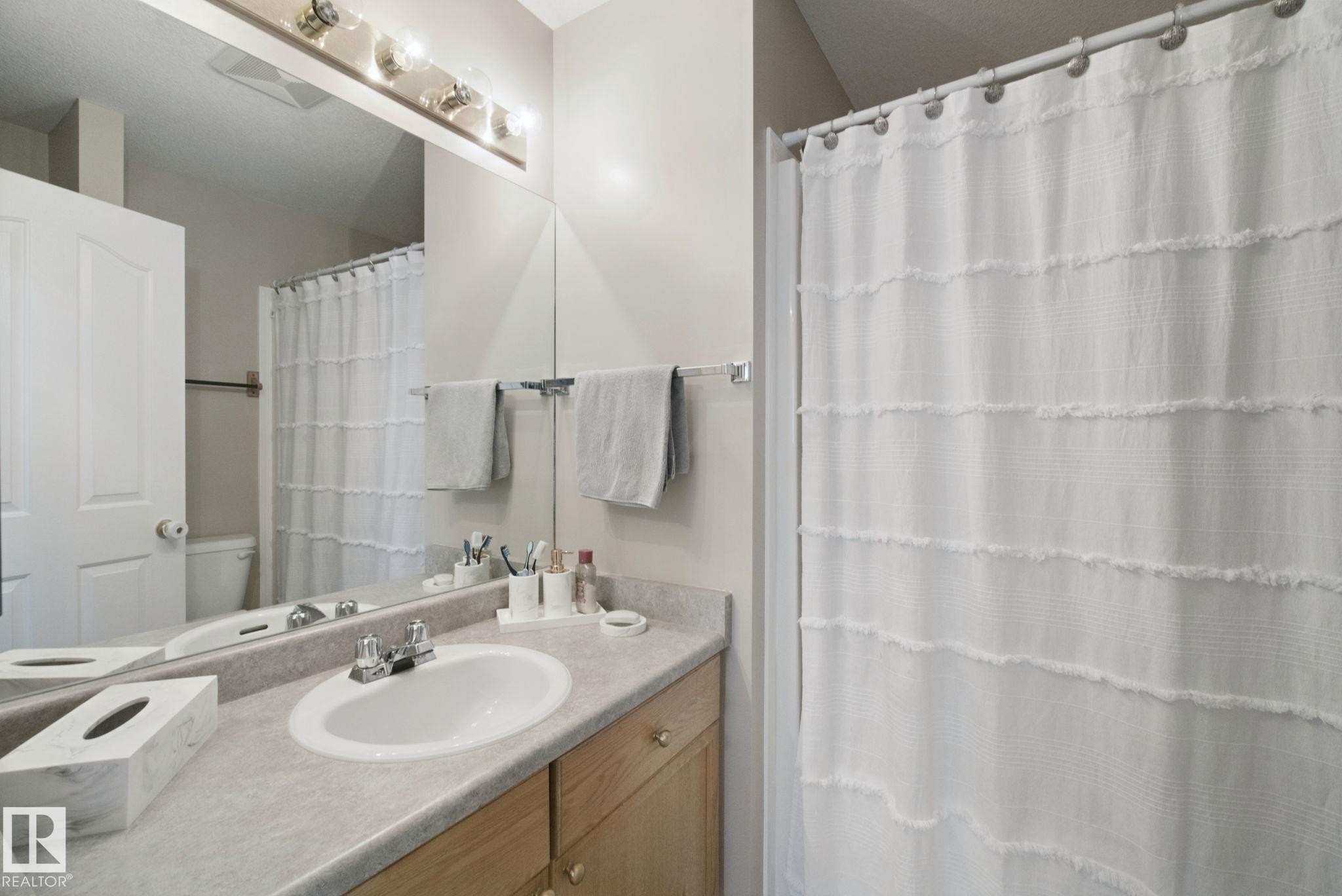 Full-width vanity mirror, integrated sink, wood-finish cabinetry, and overhead vanity lighting - 13912 156 Avenue Nw, Edmonton, AB
