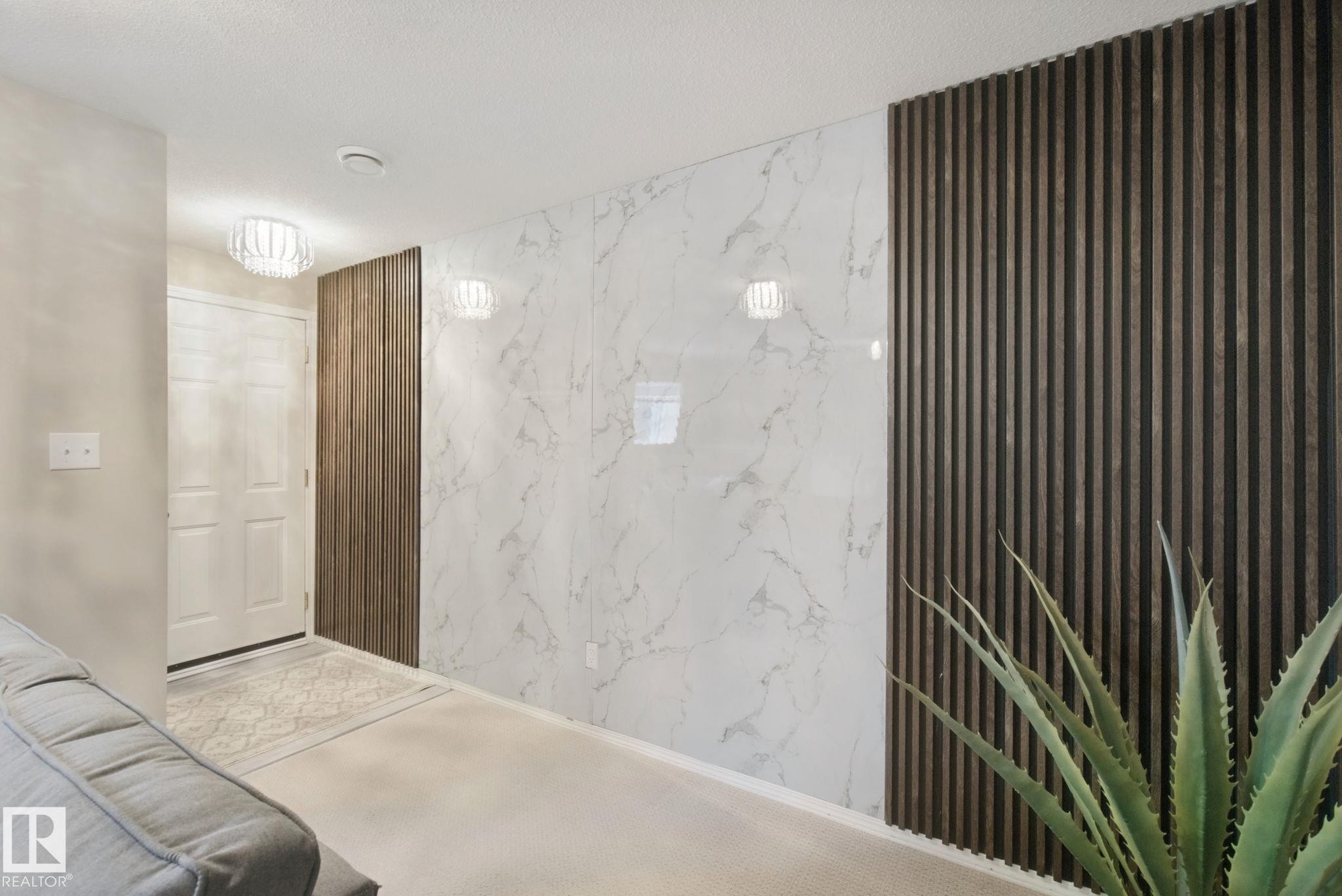 Entryway featuring a white paneled door, decorative ceiling light fixture, accent wall with vertical wood paneling, and white wall panels with grey veining - 13912 156 Avenue Nw, Edmonton, AB