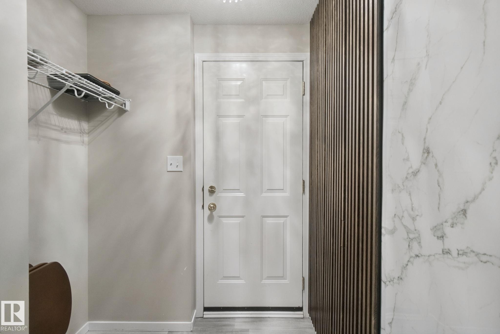 White panel door with brass hardware, wall-mounted wire shelving, and wood-slat accent wall - 13912 156 Avenue Nw, Edmonton, AB