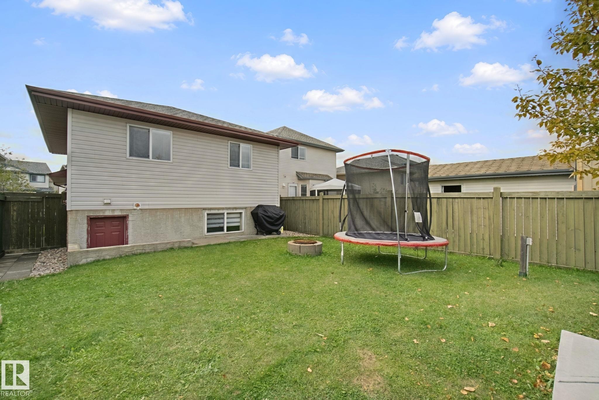 Expansive backyard featuring a manicured lawn, full privacy fencing, a concrete retaining wall, and a side access door - 13912 156 Avenue Nw, Edmonton, AB