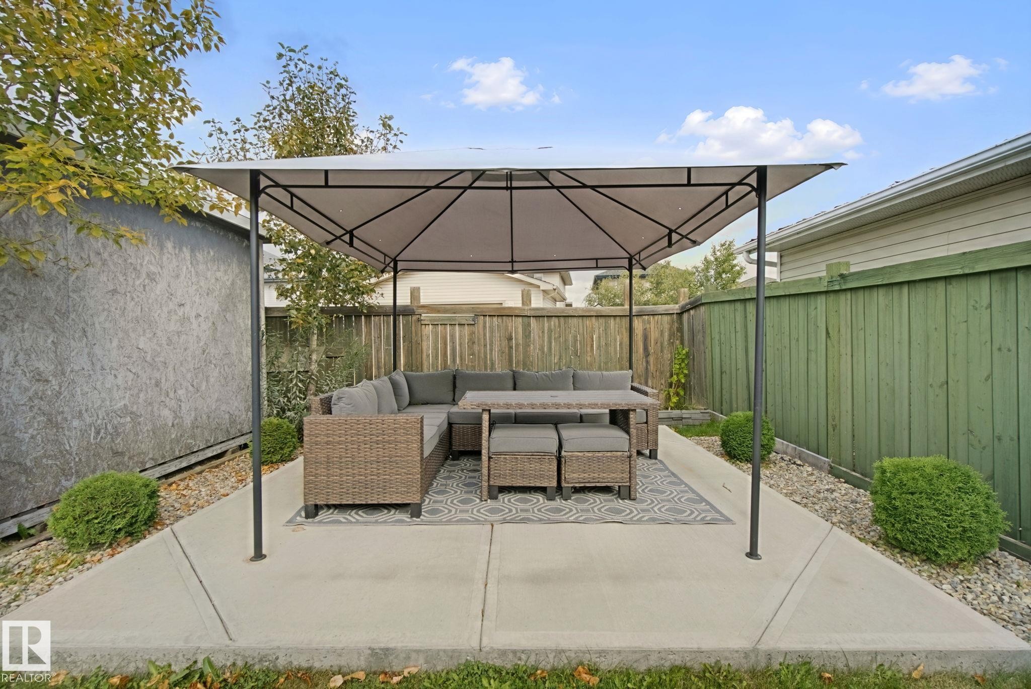 Paved patio area with a covered gazebo structure, bordered by a privacy fence and green shrubbery - 13912 156 Avenue Nw, Edmonton, AB