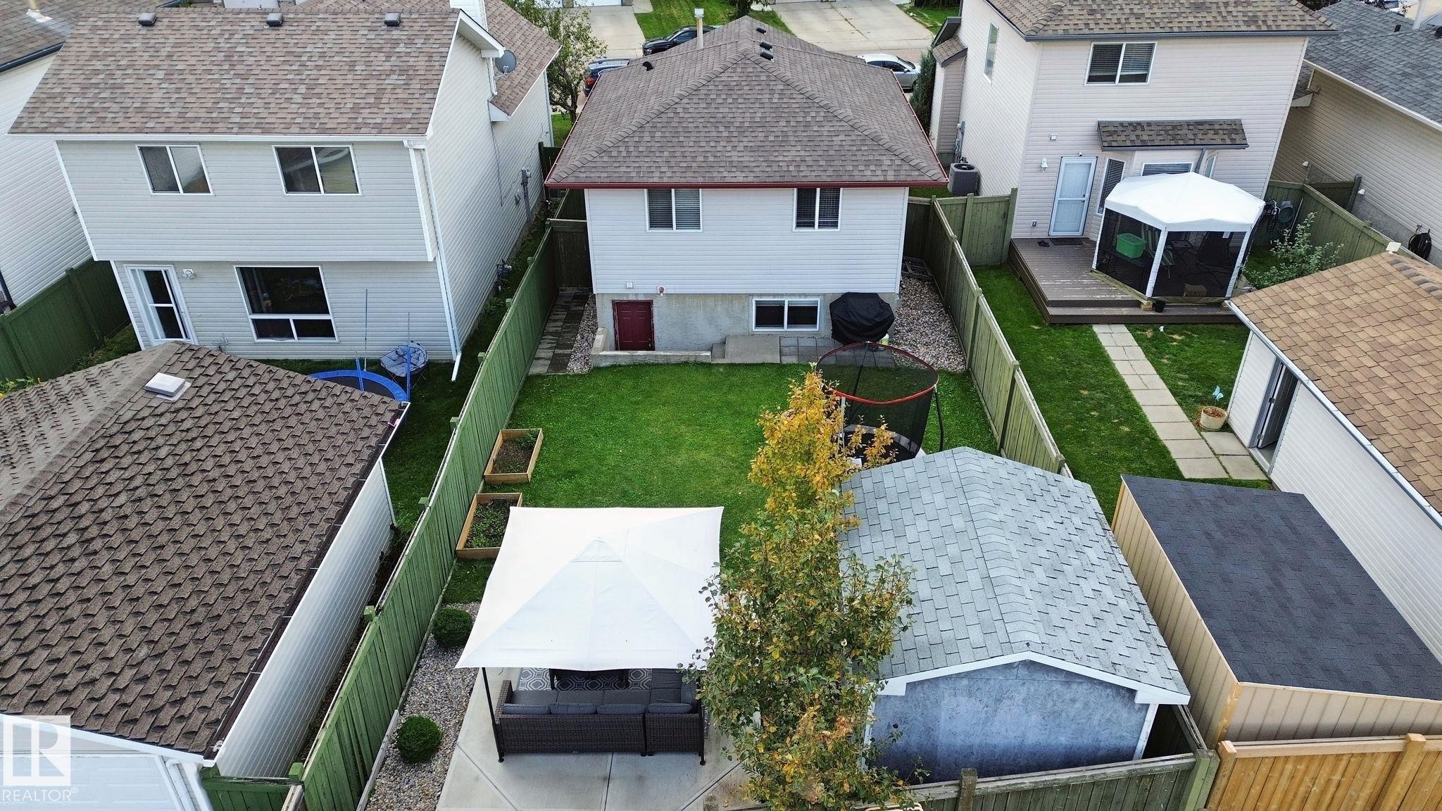 Expansive backyard featuring a green lawn, wood fencing, concrete patio, and a detached shed - 13912 156 Avenue Nw, Edmonton, AB