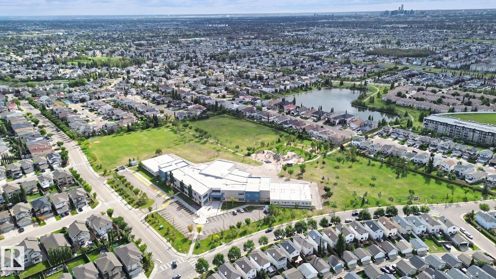 Expansive residential neighborhood featuring a central body of water, a large school facility, and numerous detached and attached residential structures - 13912 156 Avenue Nw, Edmonton, AB