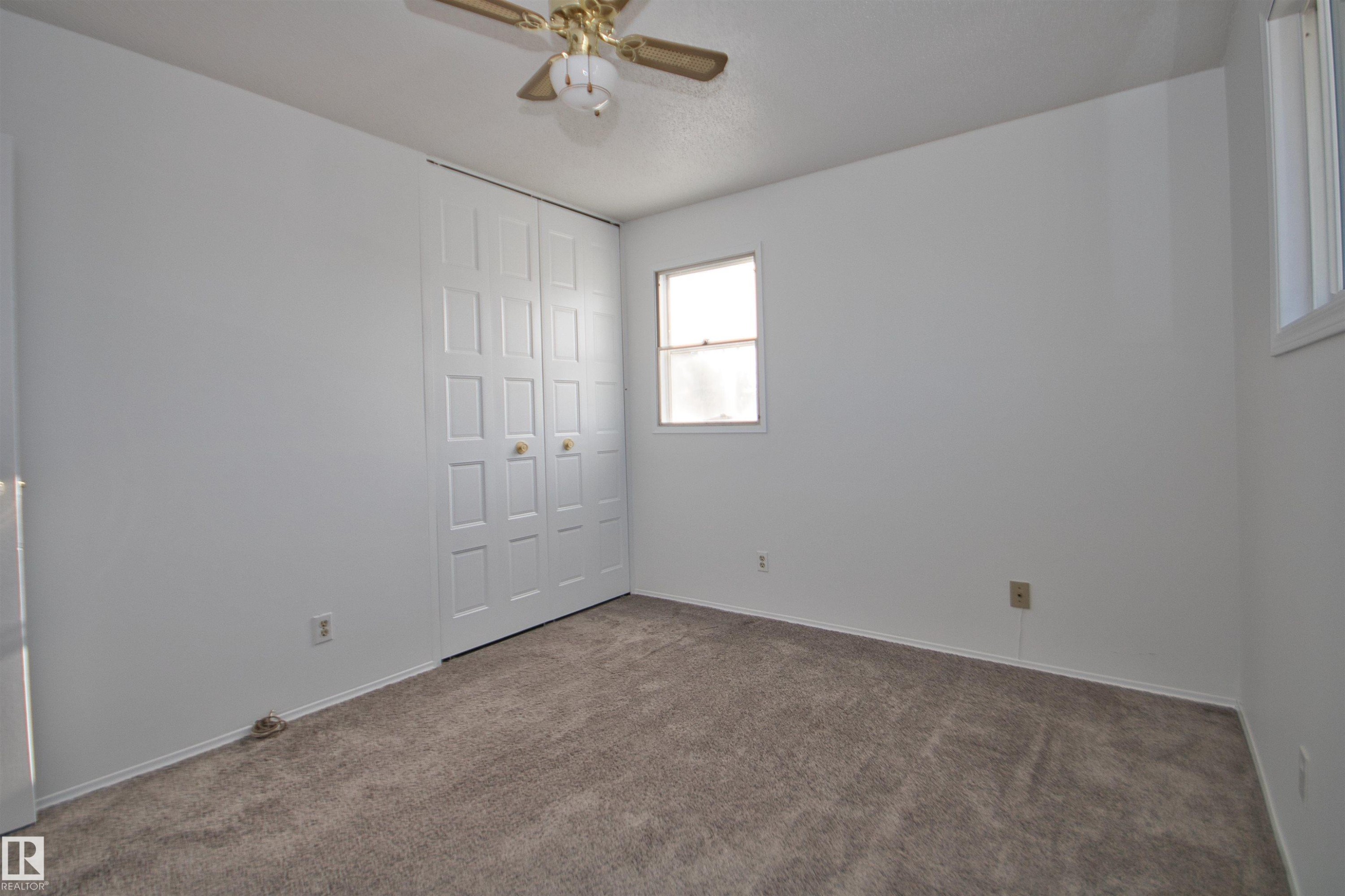 Neutral wall palette, soft carpet flooring, bi-fold closet doors, ceiling fan, and multiple windows - 7743 37 Avenue Nw, Edmonton, AB