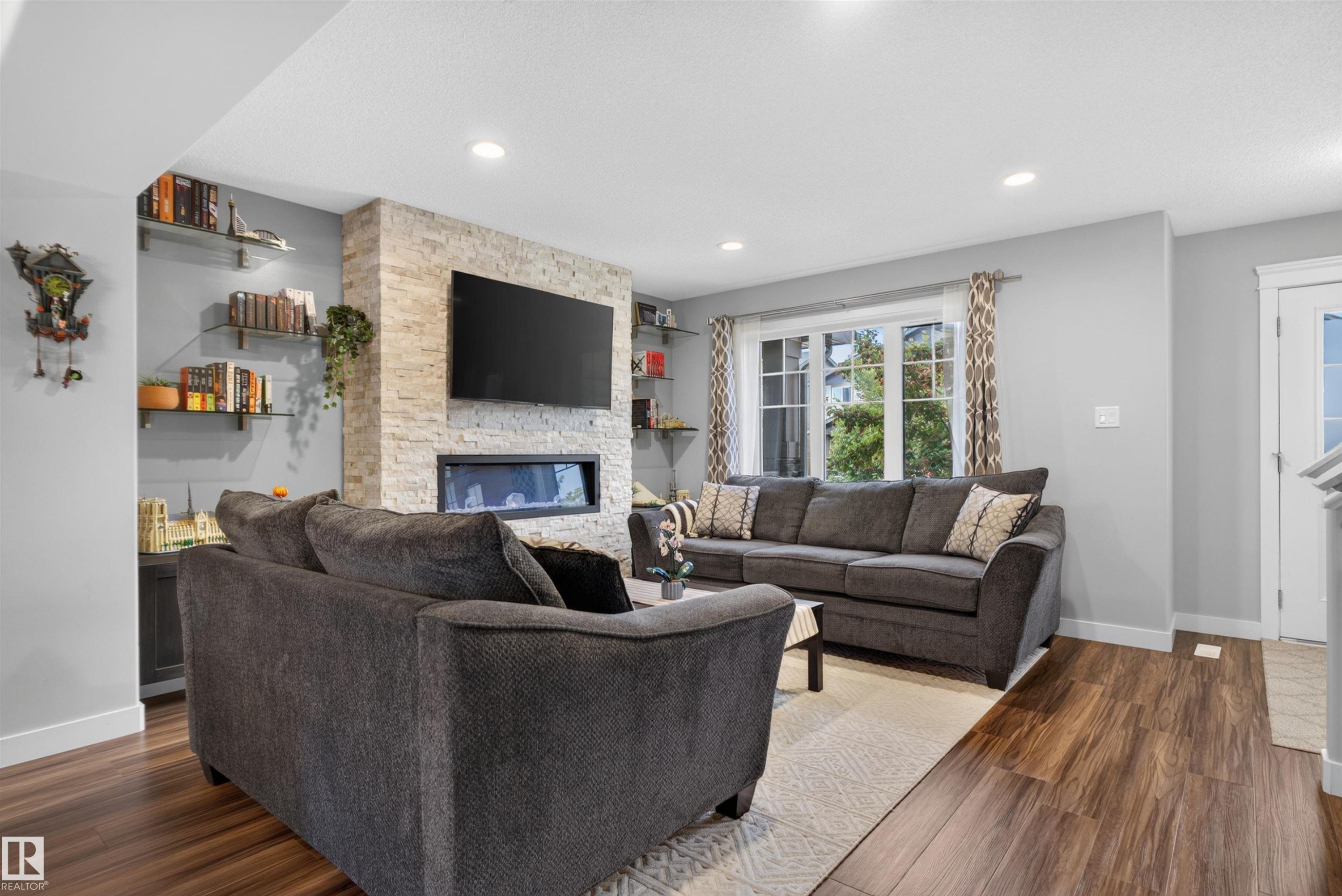 Stacked stone fireplace with a linear insert, wood-finish flooring, recessed lighting, and a multi-pane window - 319 Desrochers Boulevard Sw, Edmonton, AB