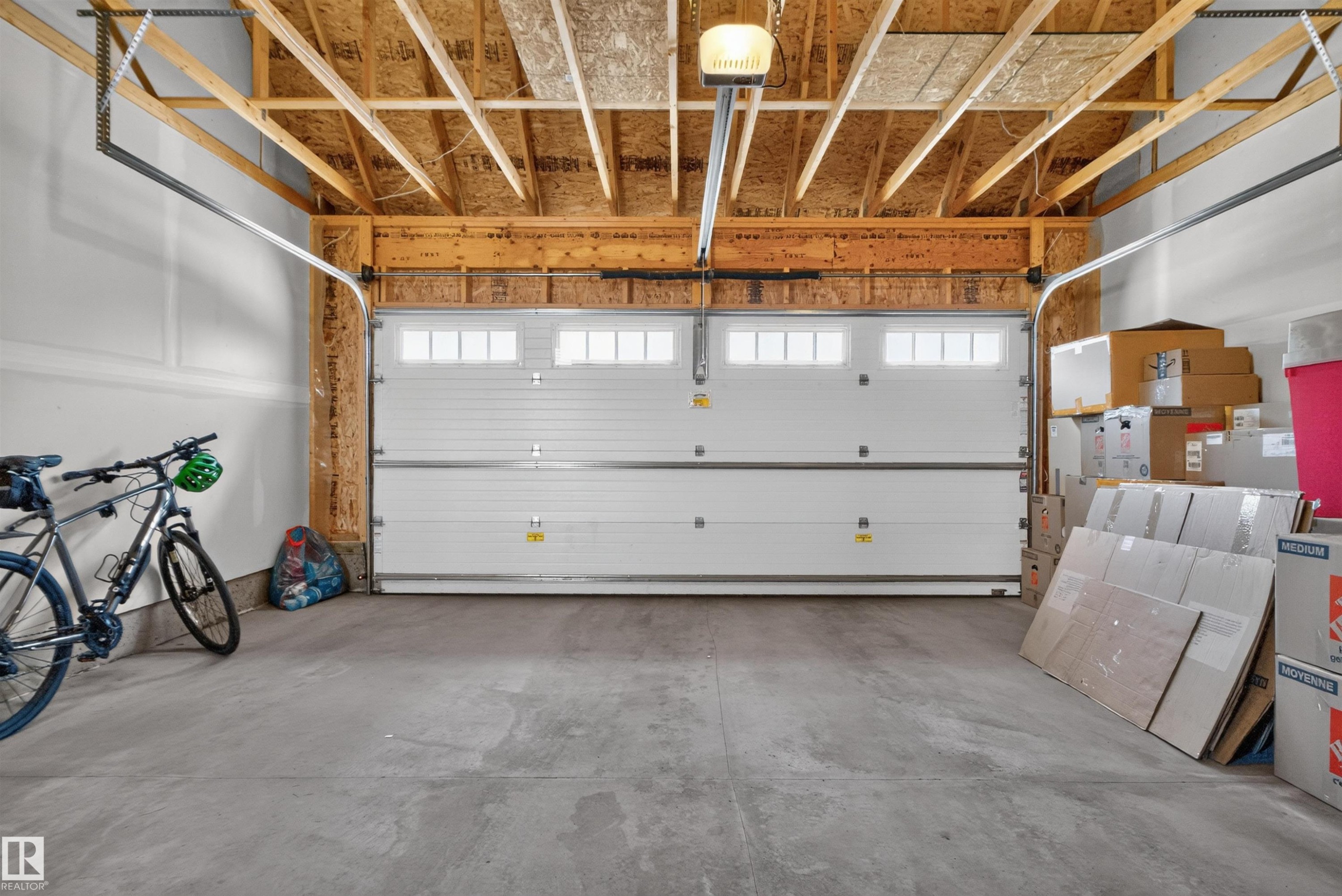 Exposed wood ceiling beams, concrete flooring, overhead garage door opener, and a white paneled garage door with upper window inserts - 319 Desrochers Boulevard Sw, Edmonton, AB