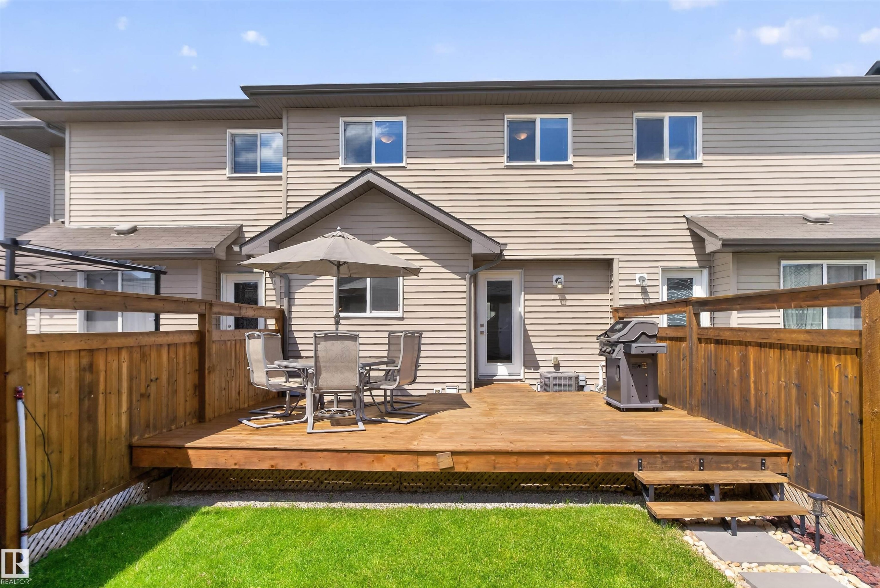 Expansive wood deck with stairs to a manicured lawn, complemented by a privacy fence and vinyl siding exterior - 319 Desrochers Boulevard Sw, Edmonton, AB