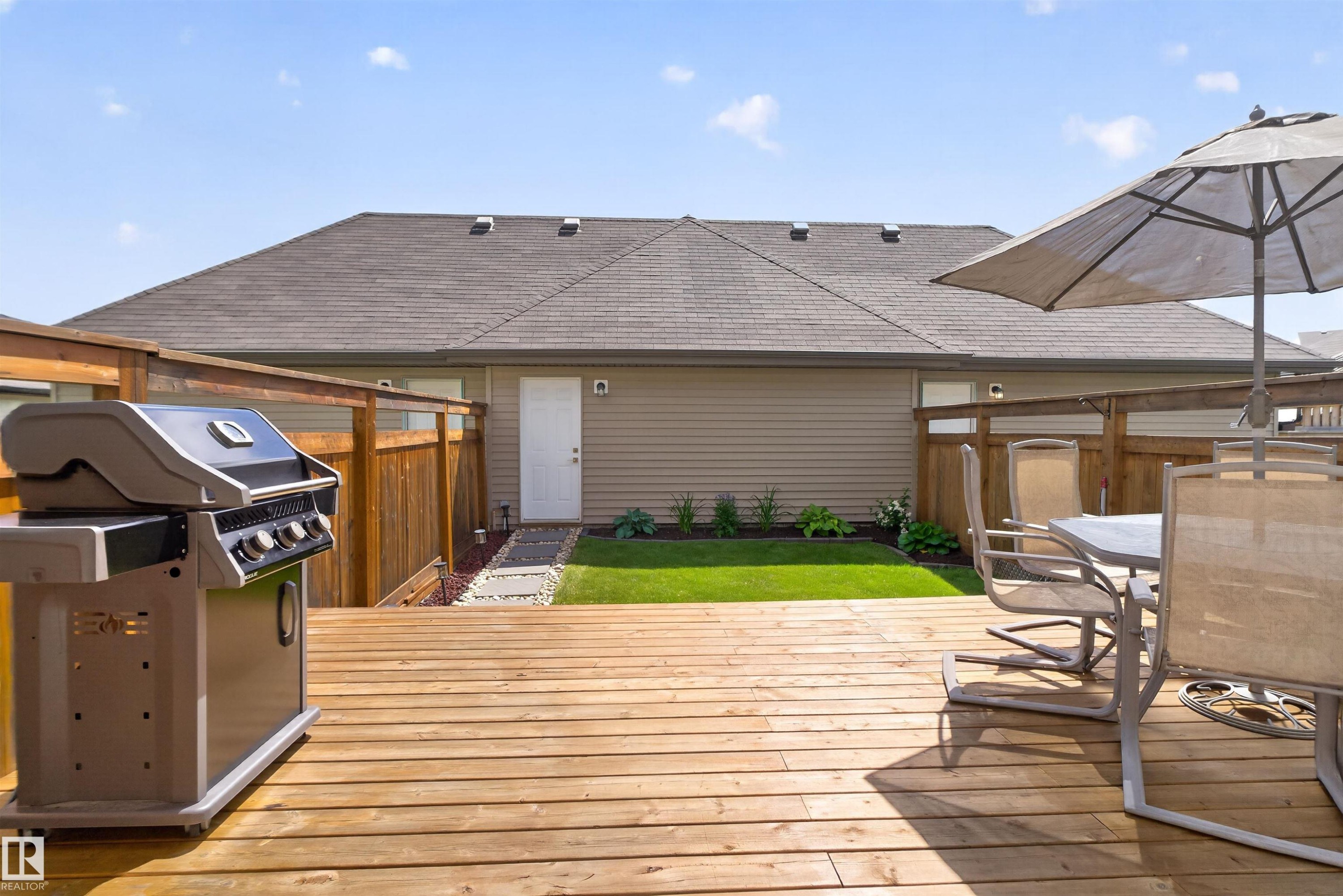 Expansive wood deck with a partial privacy fence, leading to a manicured lawn and garden bed - 319 Desrochers Boulevard Sw, Edmonton, AB