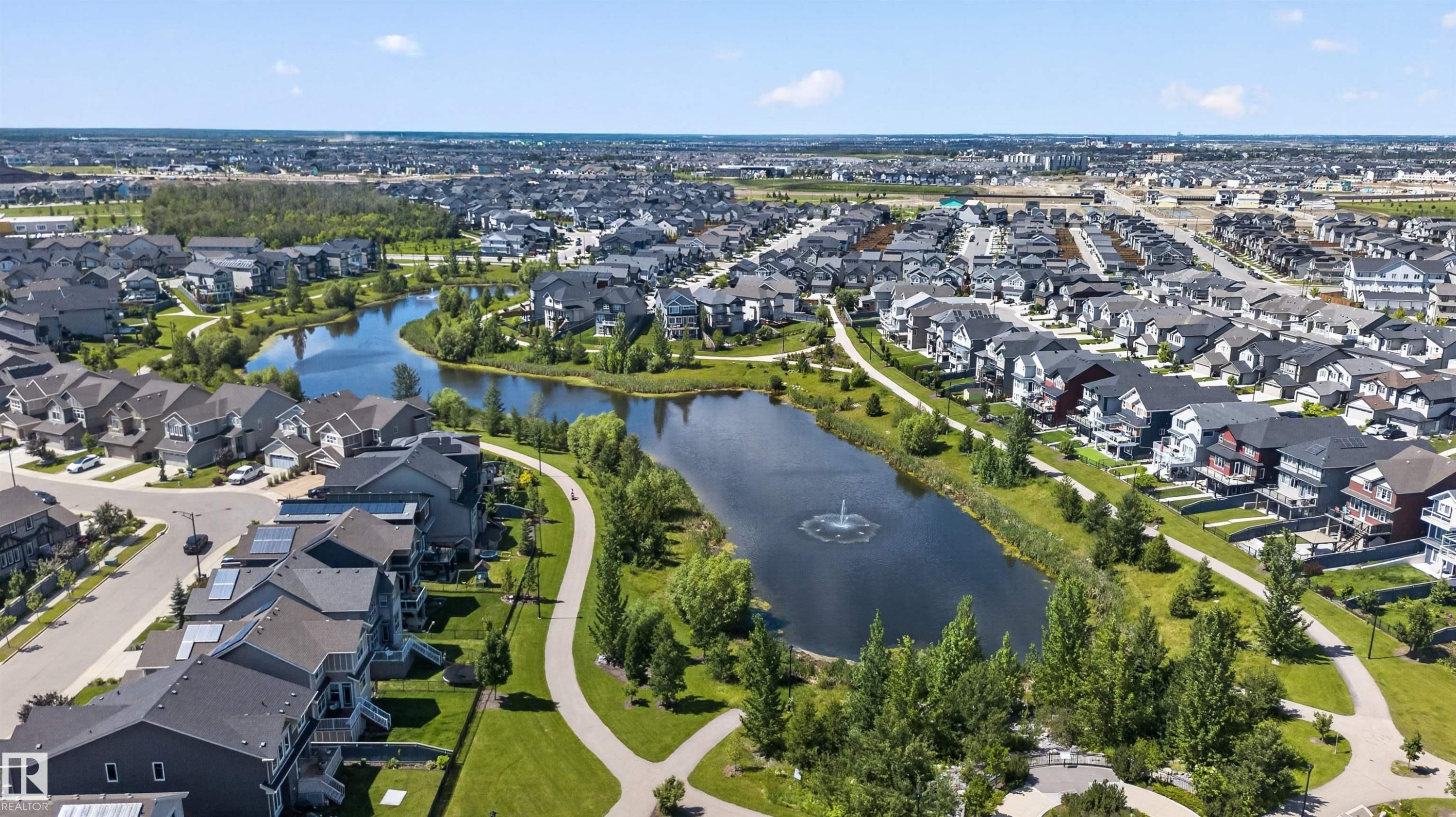 Residential community featuring a central pond with a fountain, paved walking paths, established green spaces, and mature trees - 319 Desrochers Boulevard Sw, Edmonton, AB