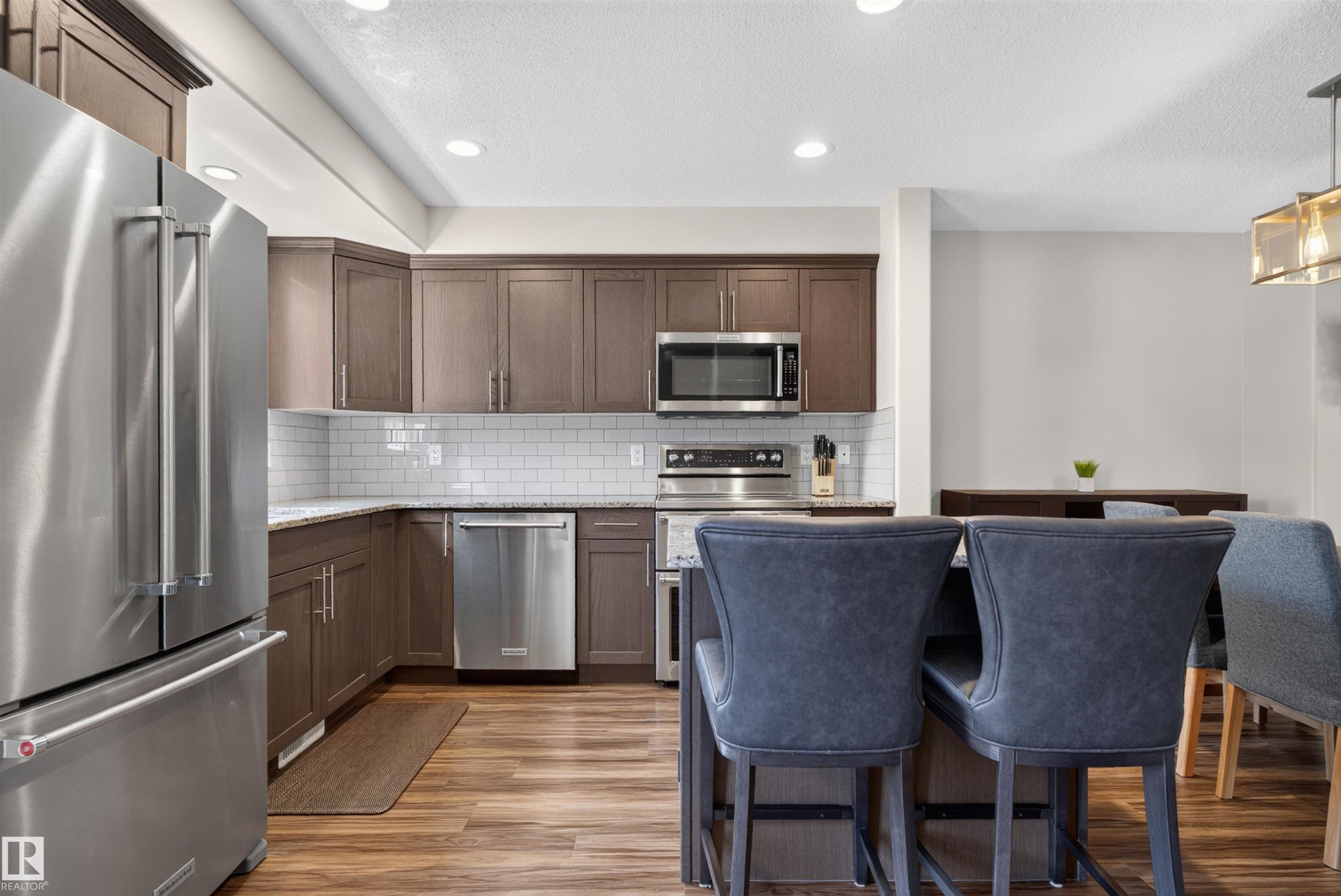 Kitchen featuring stainless steel appliances, wood-finish flooring, recessed lighting, white subway tile backsplash, and dark wood cabinetry - 319 Desrochers Boulevard Sw, Edmonton, AB