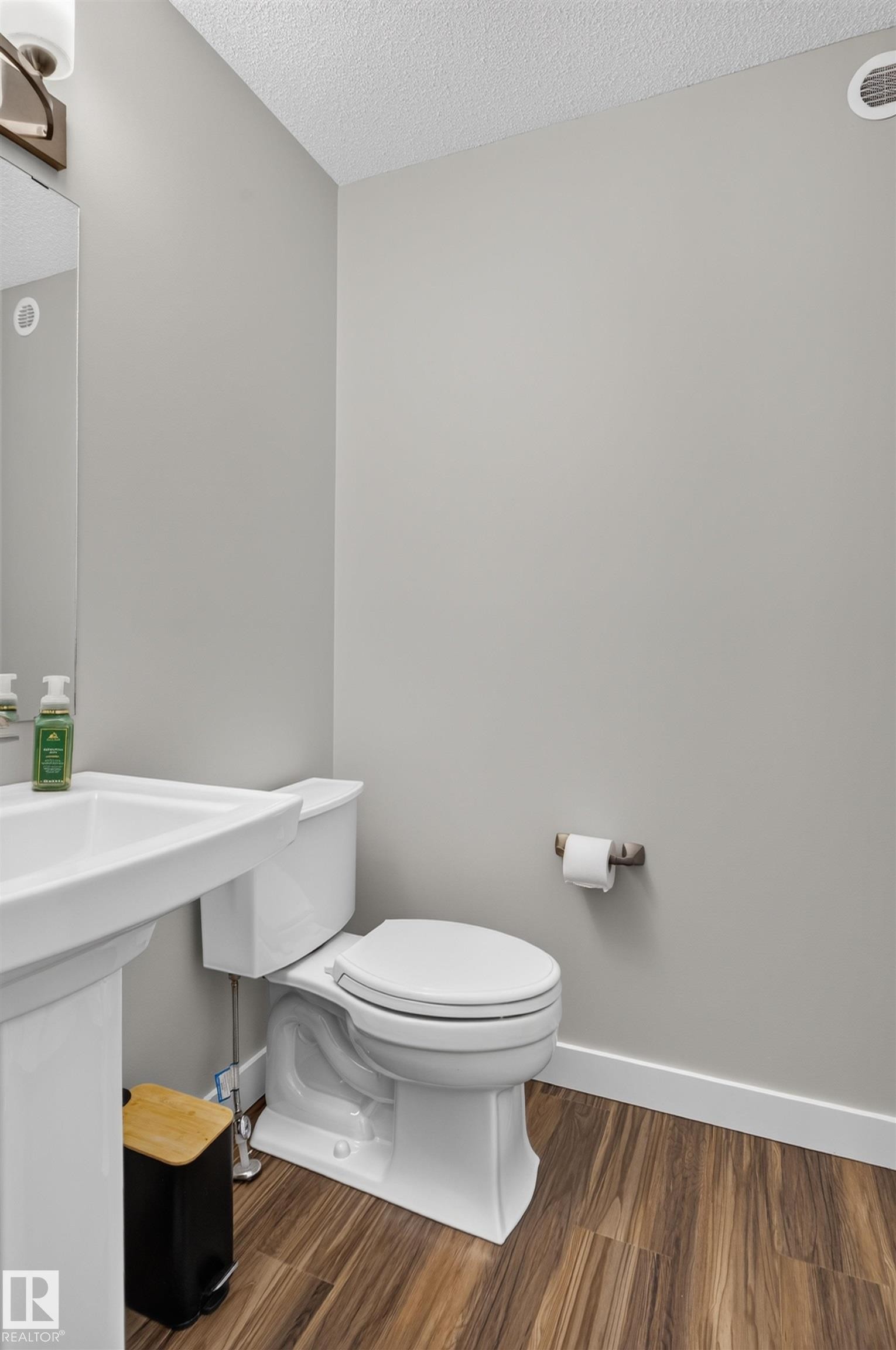 Pedestal sink with a wall-mounted mirror, wood-finish flooring, and a contemporary toilet - 319 Desrochers Boulevard Sw, Edmonton, AB