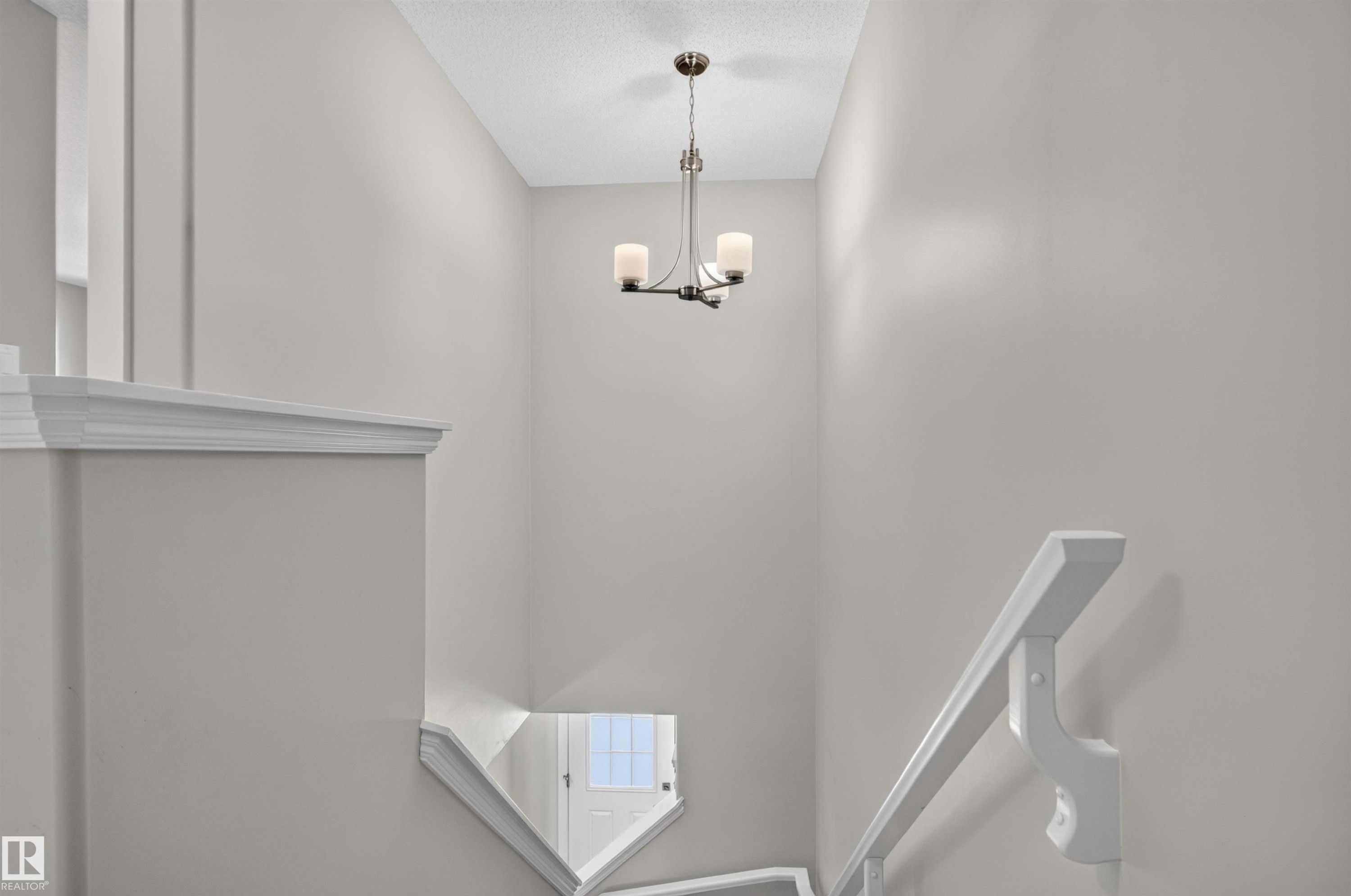 Recessed staircase with white railings, a minimalist chandelier, and light-toned wall finishes - 319 Desrochers Boulevard Sw, Edmonton, AB