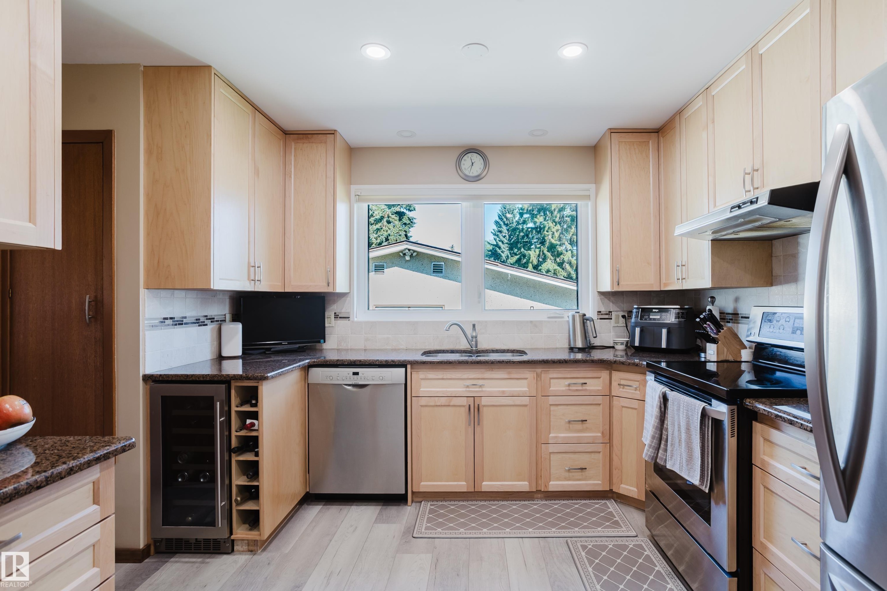 U-shaped kitchen with light wood cabinetry, stone countertops, stainless steel appliances, a built-in wine refrigerator, and wood-finish flooring - 10924 35A Avenue Nw, Edmonton, AB