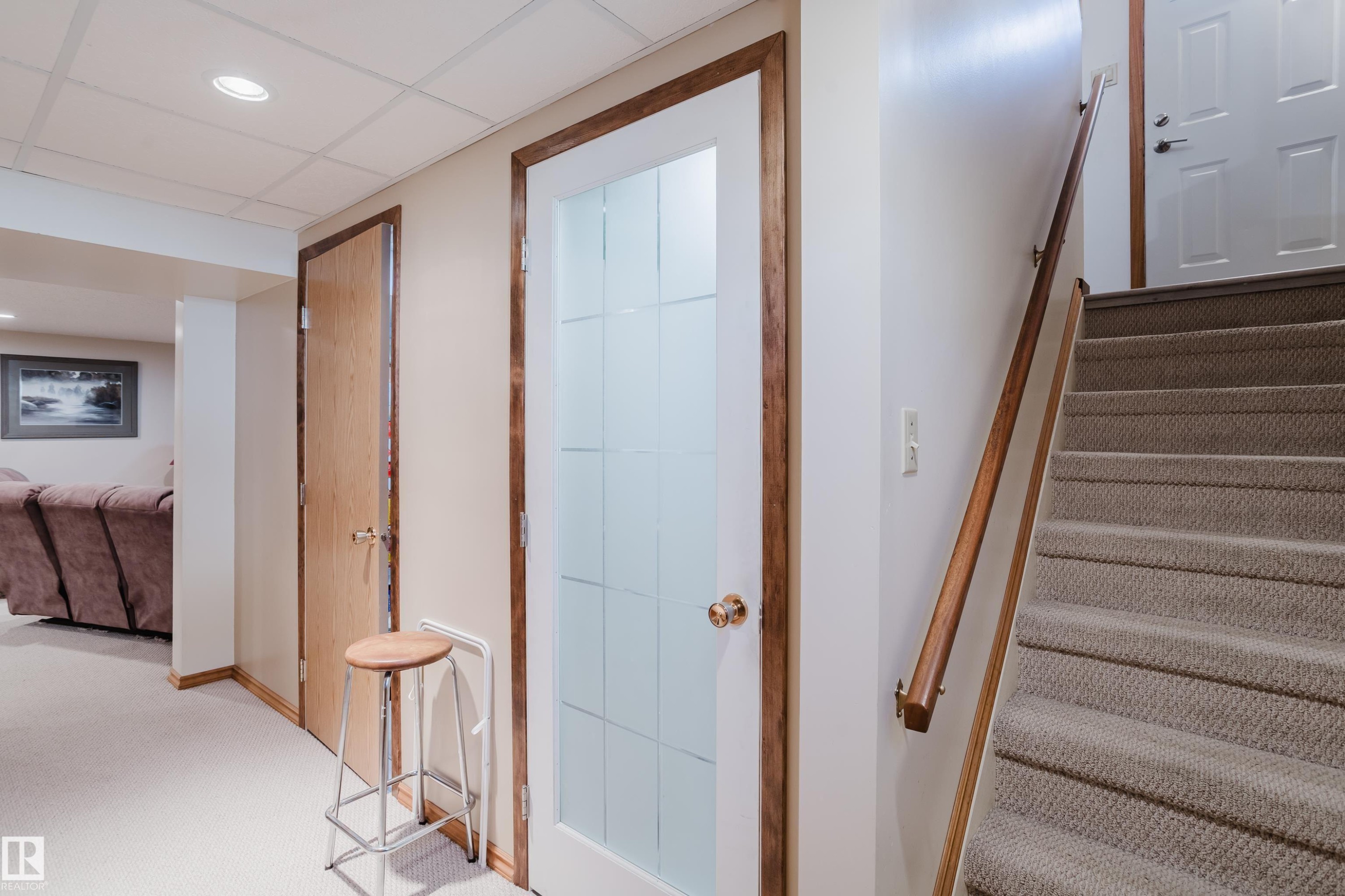 Carpeted staircase with a wood handrail, recessed ceiling lighting, and a door with frosted glass panels - 10924 35A Avenue Nw, Edmonton, AB
