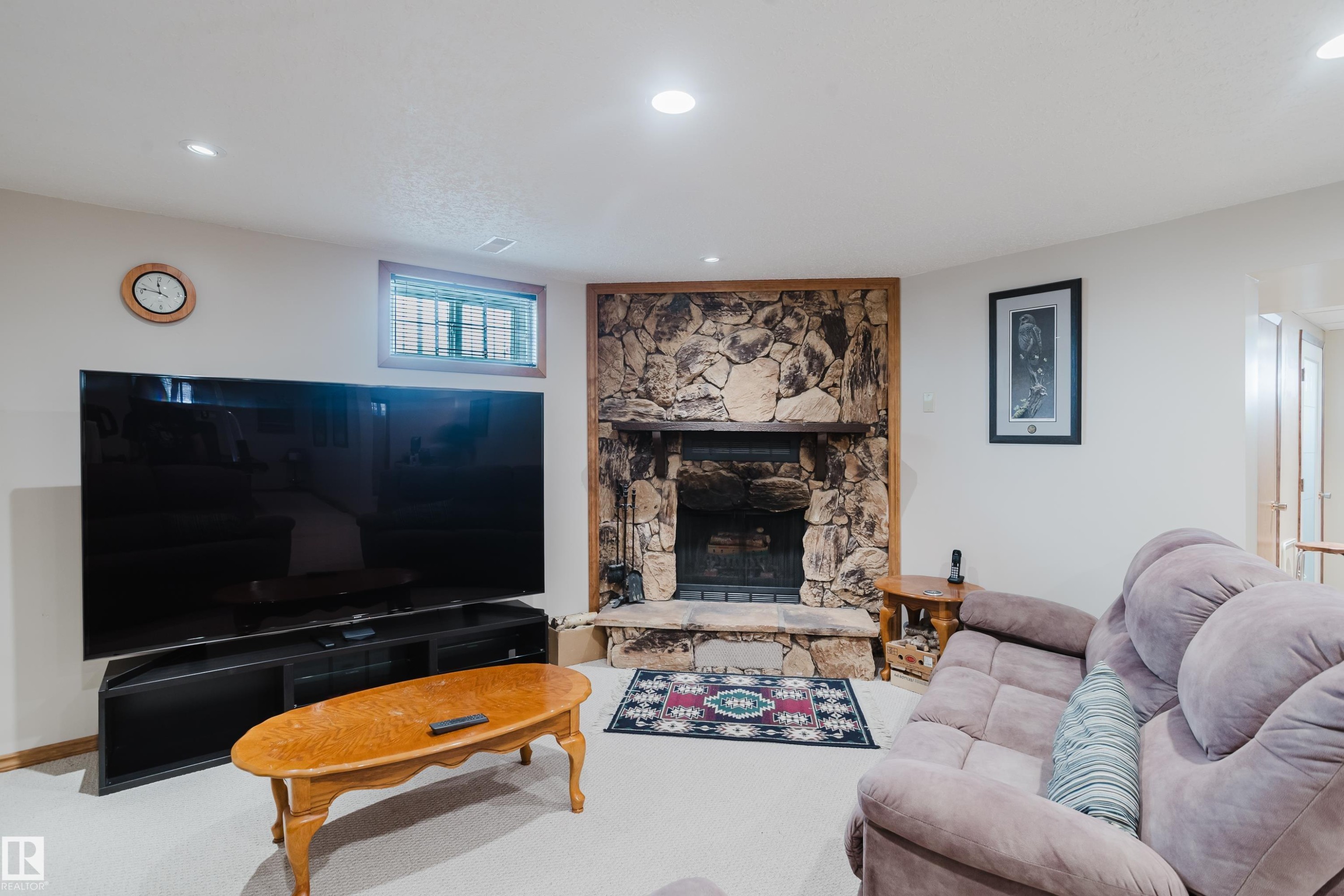 Stone fireplace with hearth, recessed lighting, wood-trimmed window, and neutral carpeting - 10924 35A Avenue Nw, Edmonton, AB