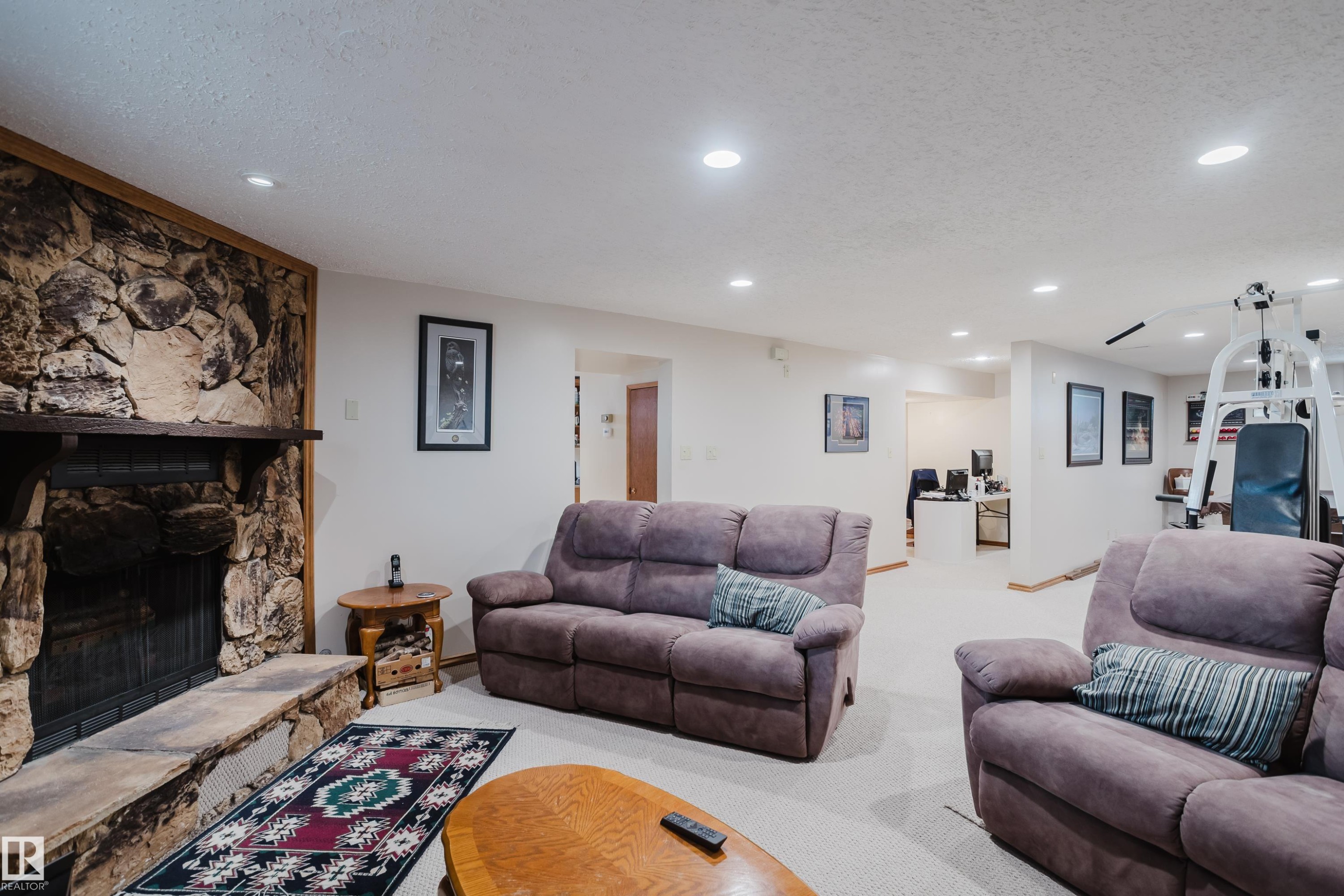 Spacious recreation area featuring a natural stone fireplace with a wood mantle, recessed lighting, and light-colored carpeting - 10924 35A Avenue Nw, Edmonton, AB