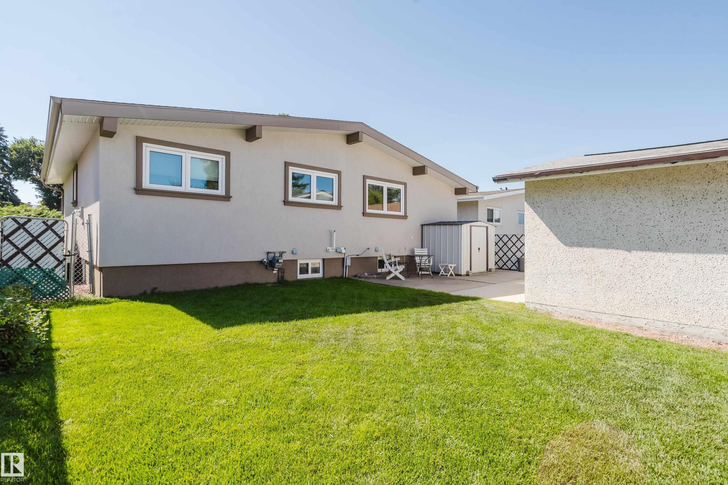Spacious backyard with a vibrant green lawn, concrete patio, and a utility shed - 10924 35A Avenue Nw, Edmonton, AB